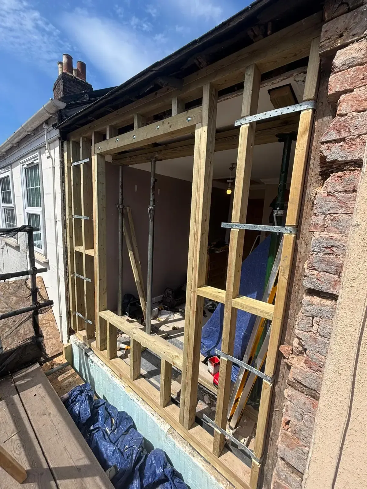 Partially built house wall with wooden framing, brickwork, and a ladder on the outside.