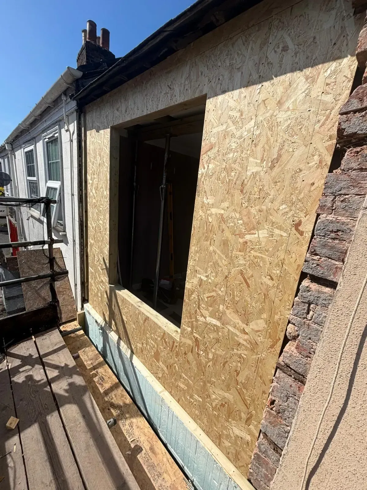 House exterior with a boarded-up window and construction materials on scaffolding