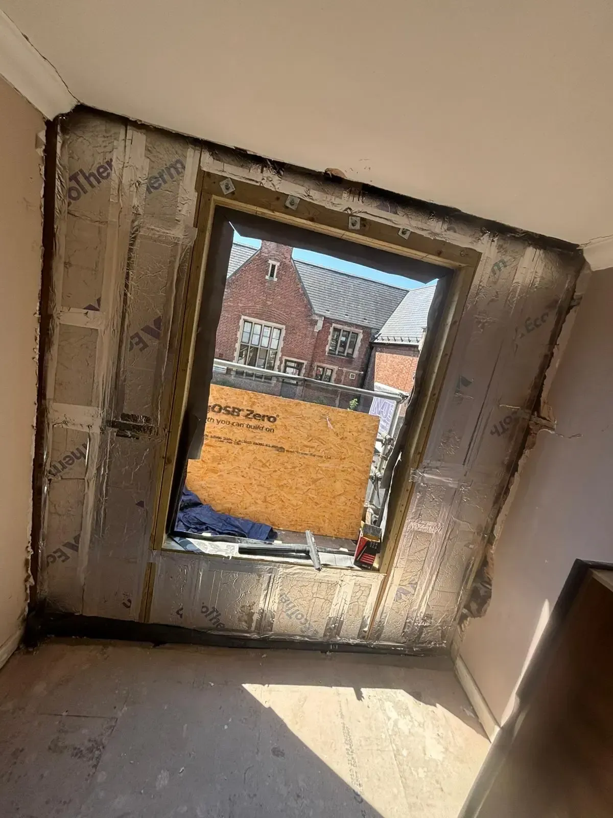 Empty room with unfinished window opening, exposed framing, and sunlight on the floor.