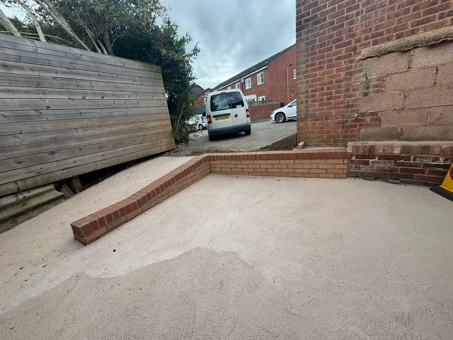 Backyard patio with low brick steps, gravel ground, and a parked van beyond a wooden fence