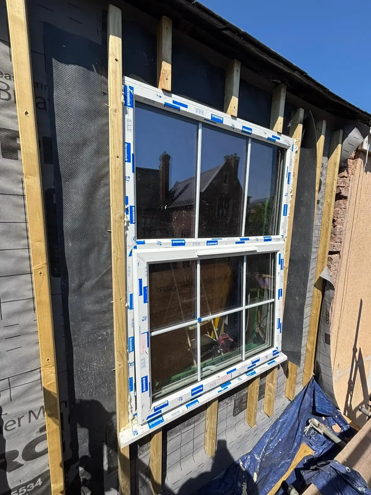 Partially installed white window on an unfinished exterior wall with insulation and exposed framing