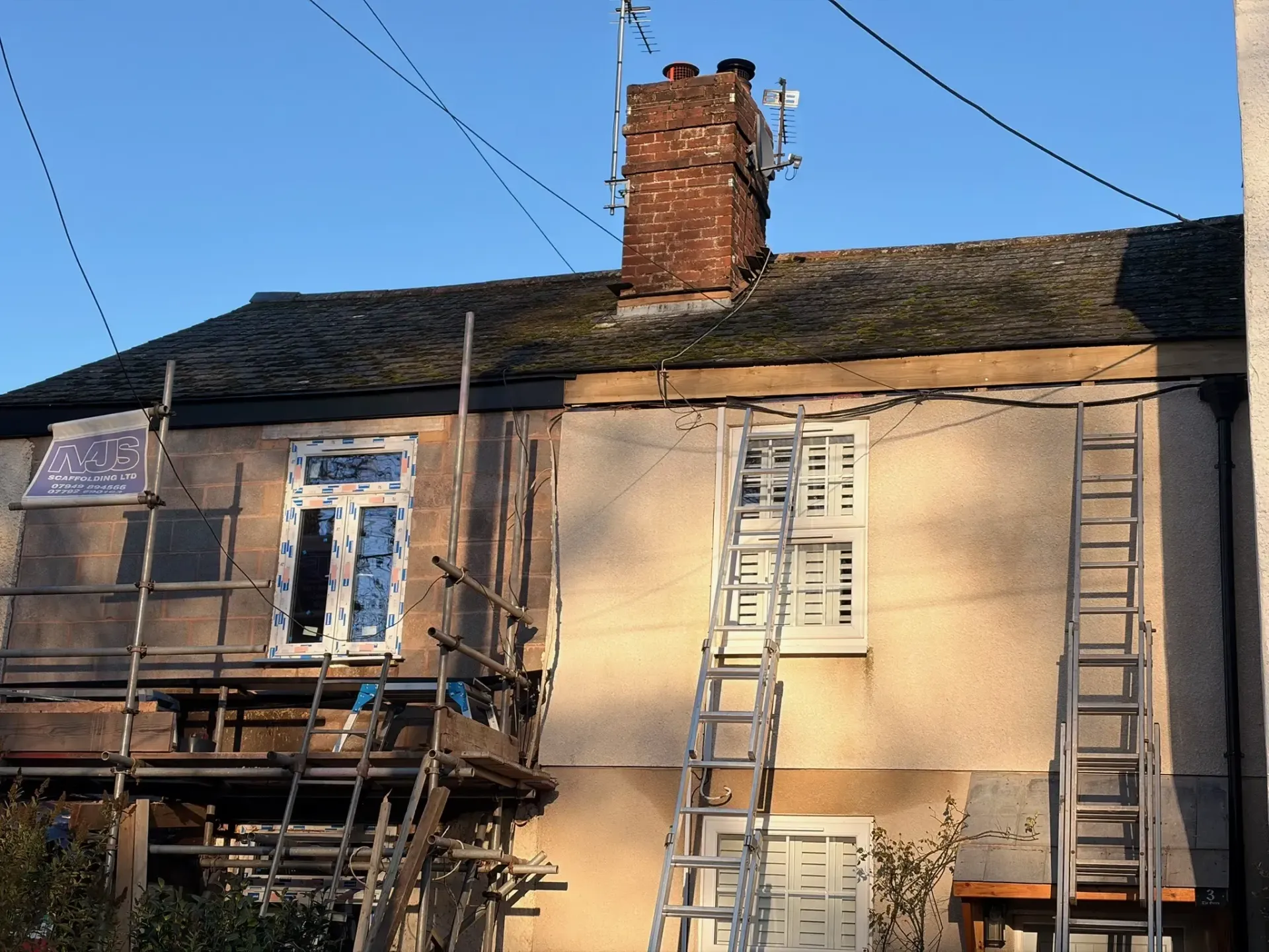 Damaged two-story house with scaffolding and ladders under a clear blue sky