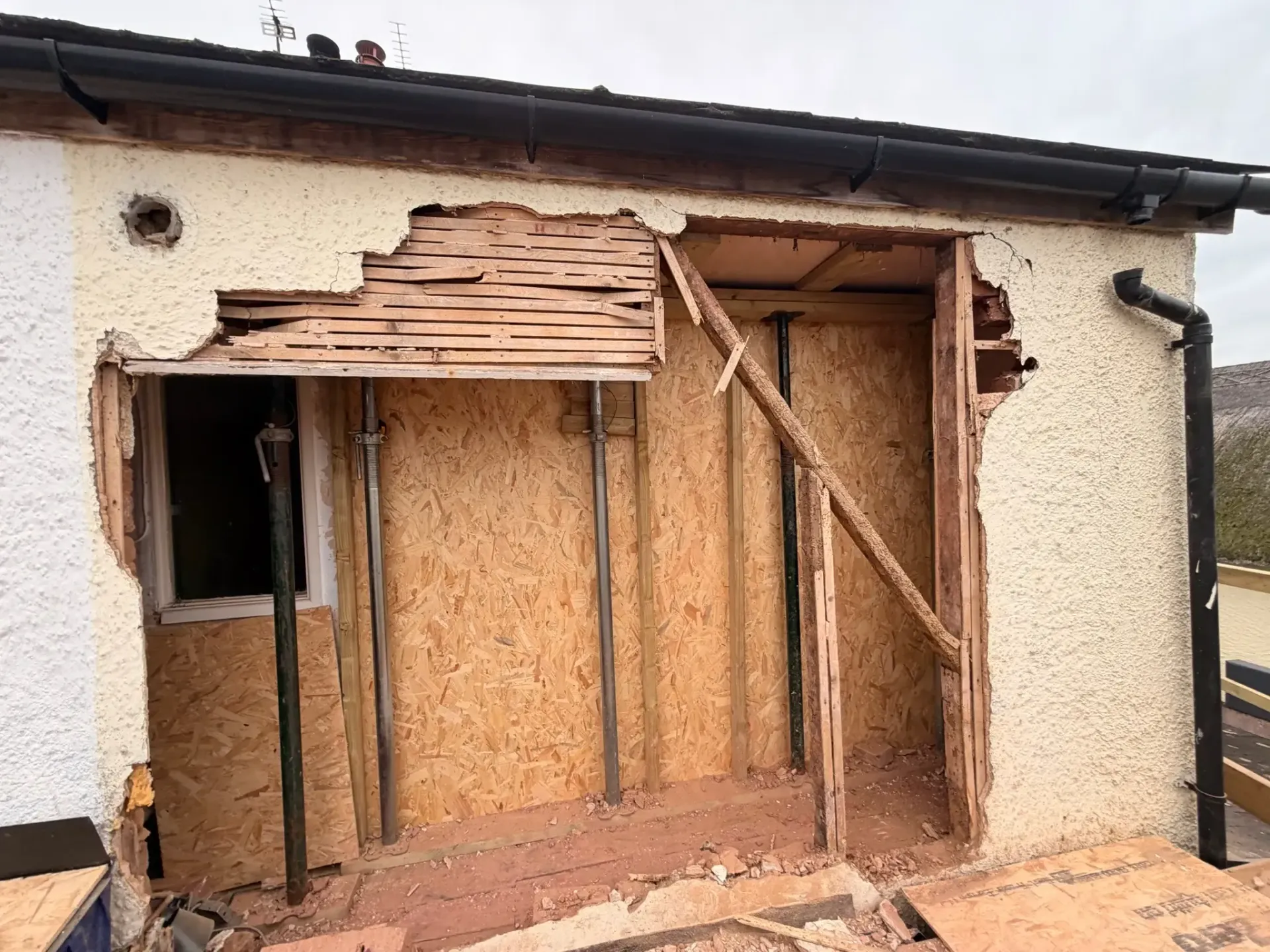 Partially demolished exterior wall of a house with exposed wooden framing and insulation boards
