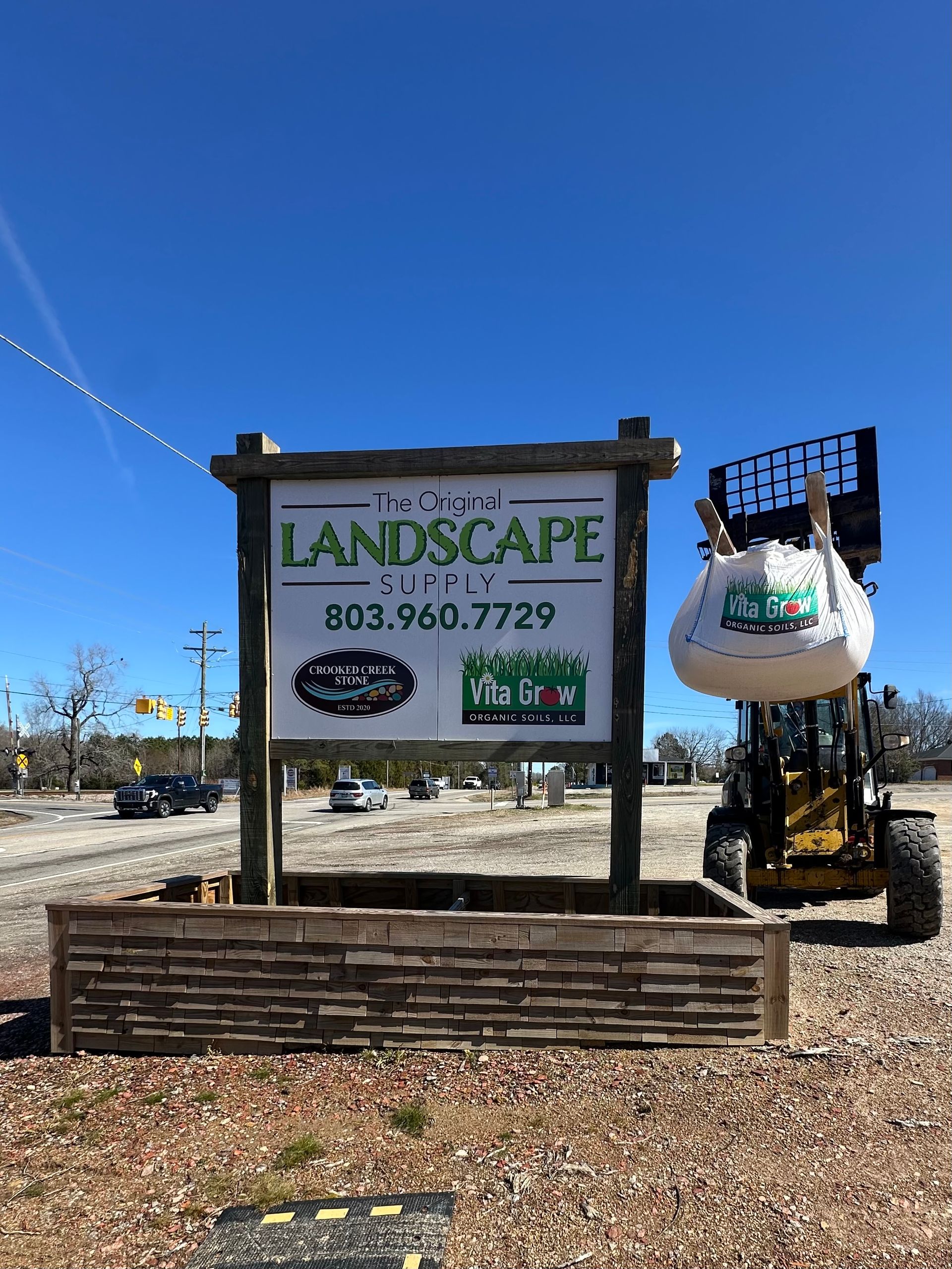 Landscaping business sign with phone number beside a decorative hanging planter outdoors on a sunny day