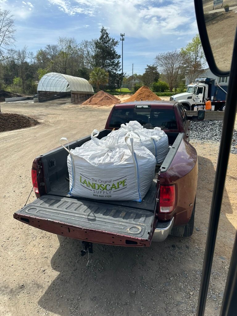 Pickup truck bed loaded with large white bags at a gravel worksite with piles of dirt and equipment
