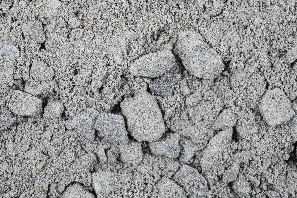 Close-up of rough gray concrete or crushed stone texture with cracks and granules