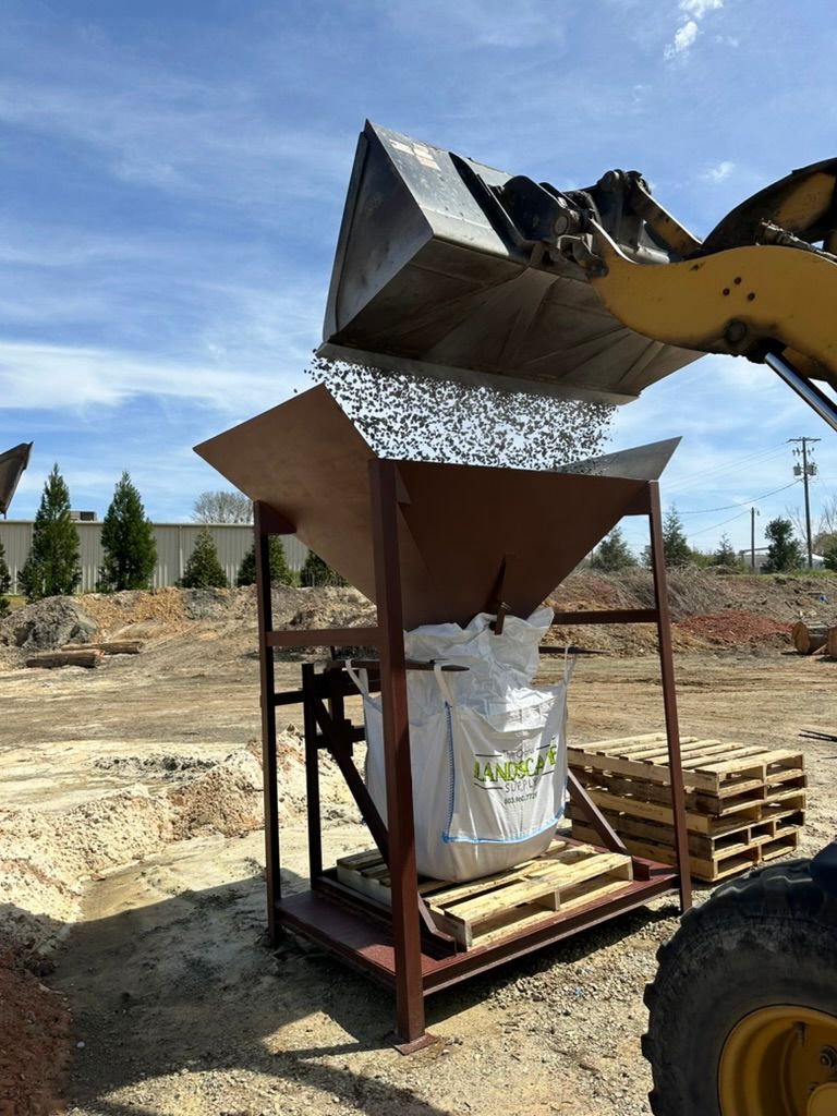 Construction equipment dumping material into a large white bag at a worksite