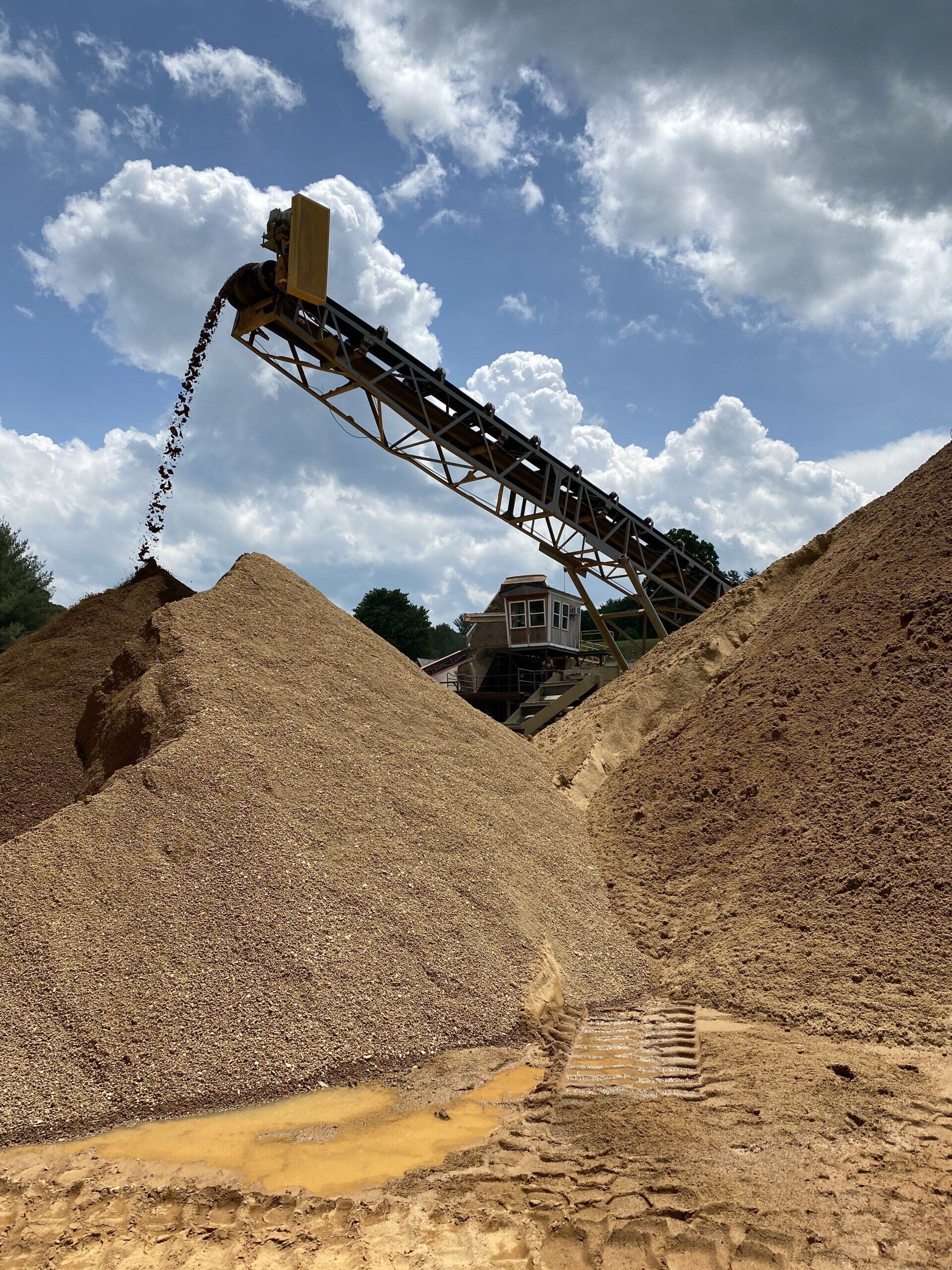 Conveyor belt dumping wood chips into large piles under a cloudy sky