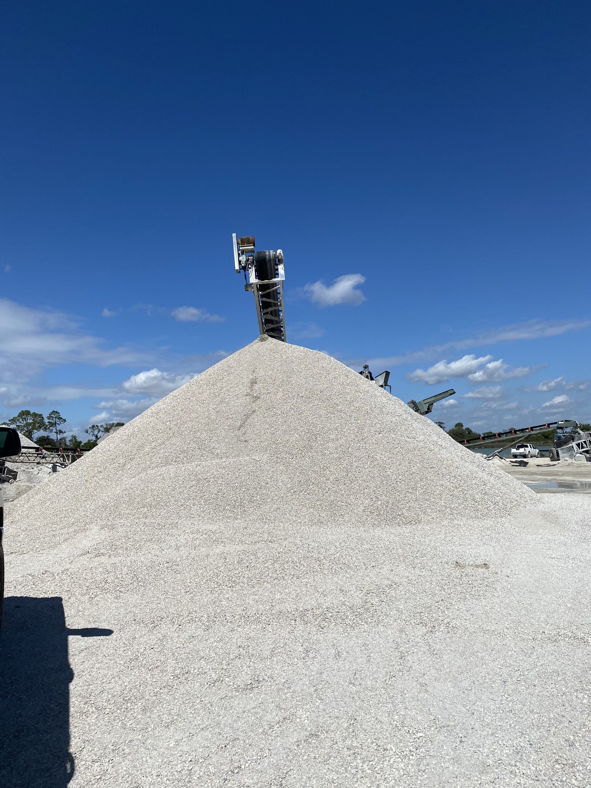 Person standing atop a large white gravel mound under a clear blue sky