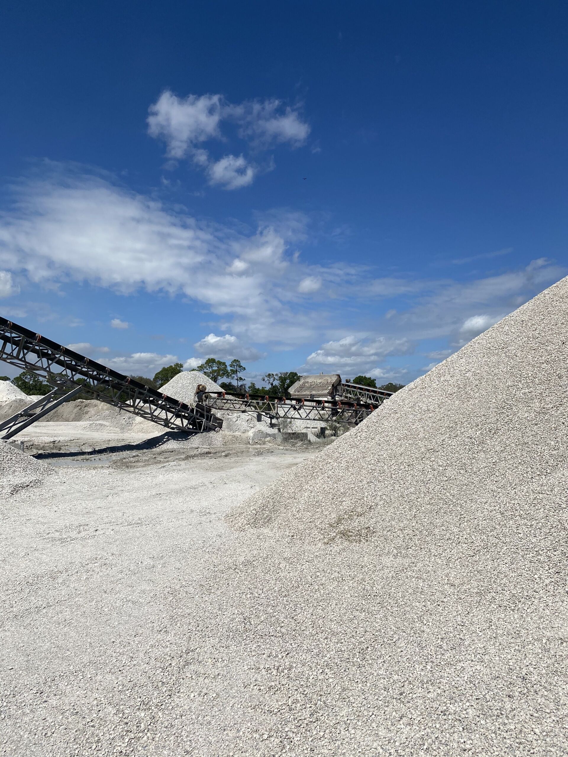 Large gravel piles at a quarry under a blue sky with clouds