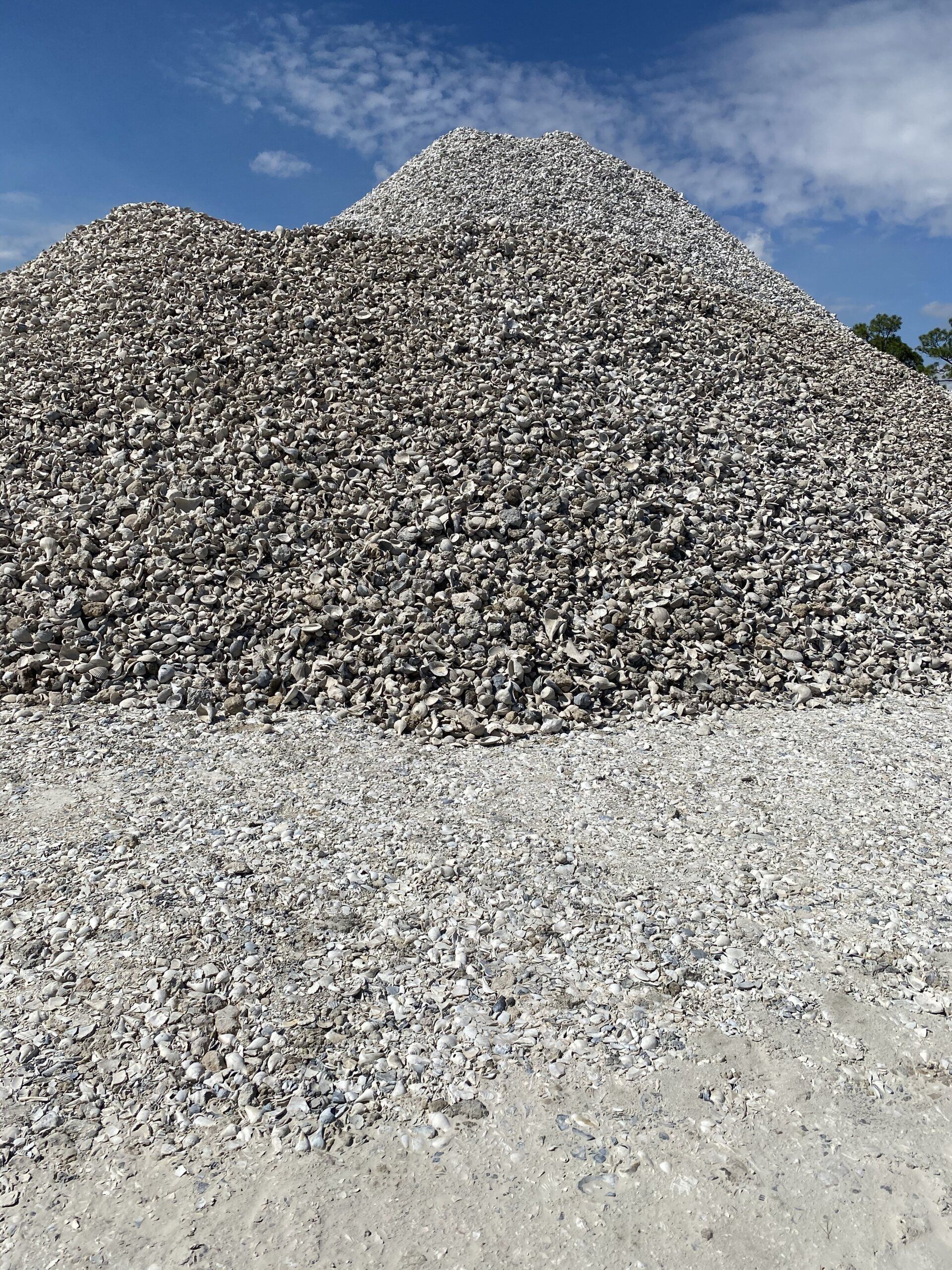 Large mound of gray gravel or rubble under a blue sky with a pale gravel foreground