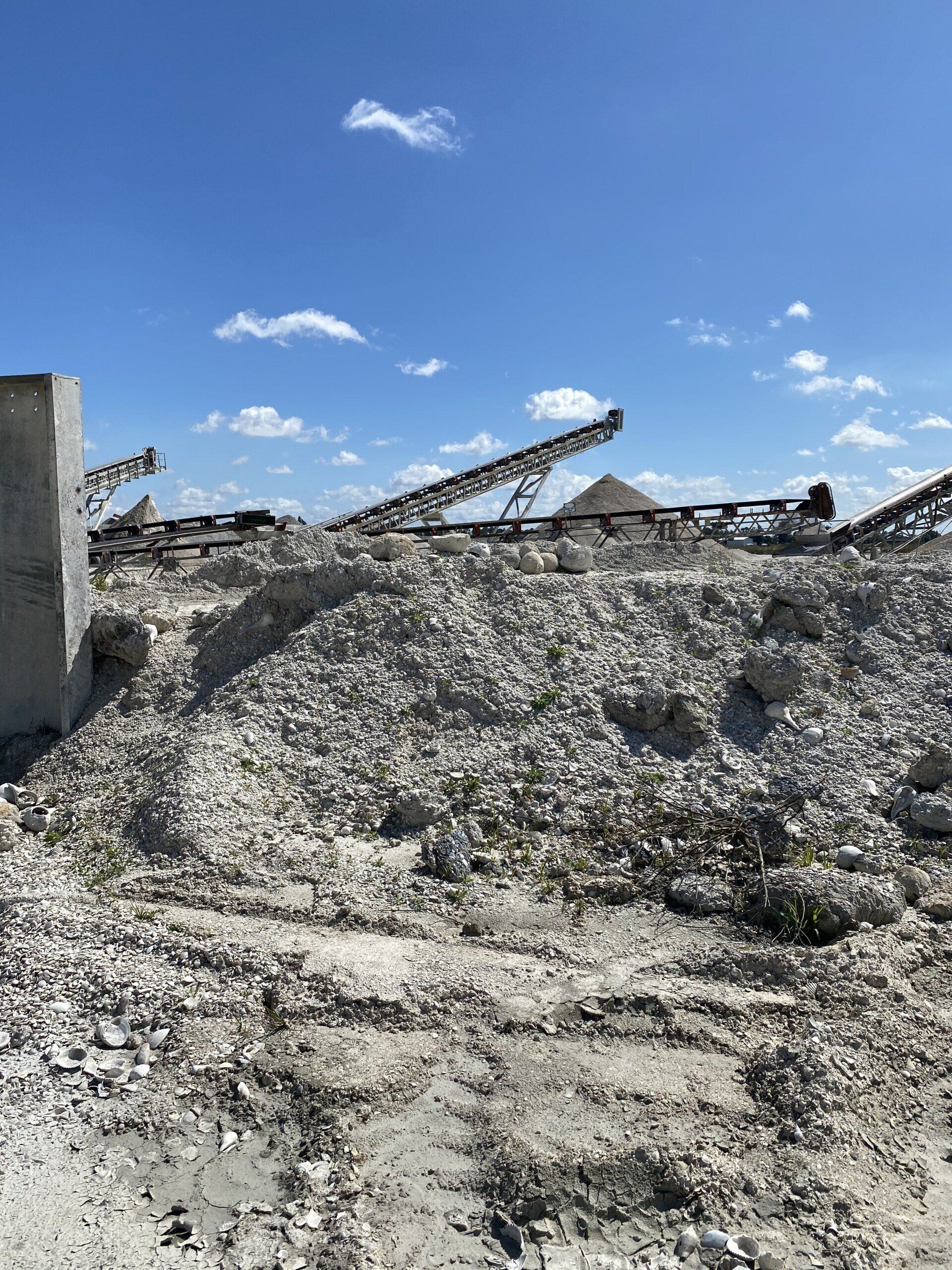 Rubble and wreckage under a bright blue sky, with a damaged structure and conveyor-like beam in the background