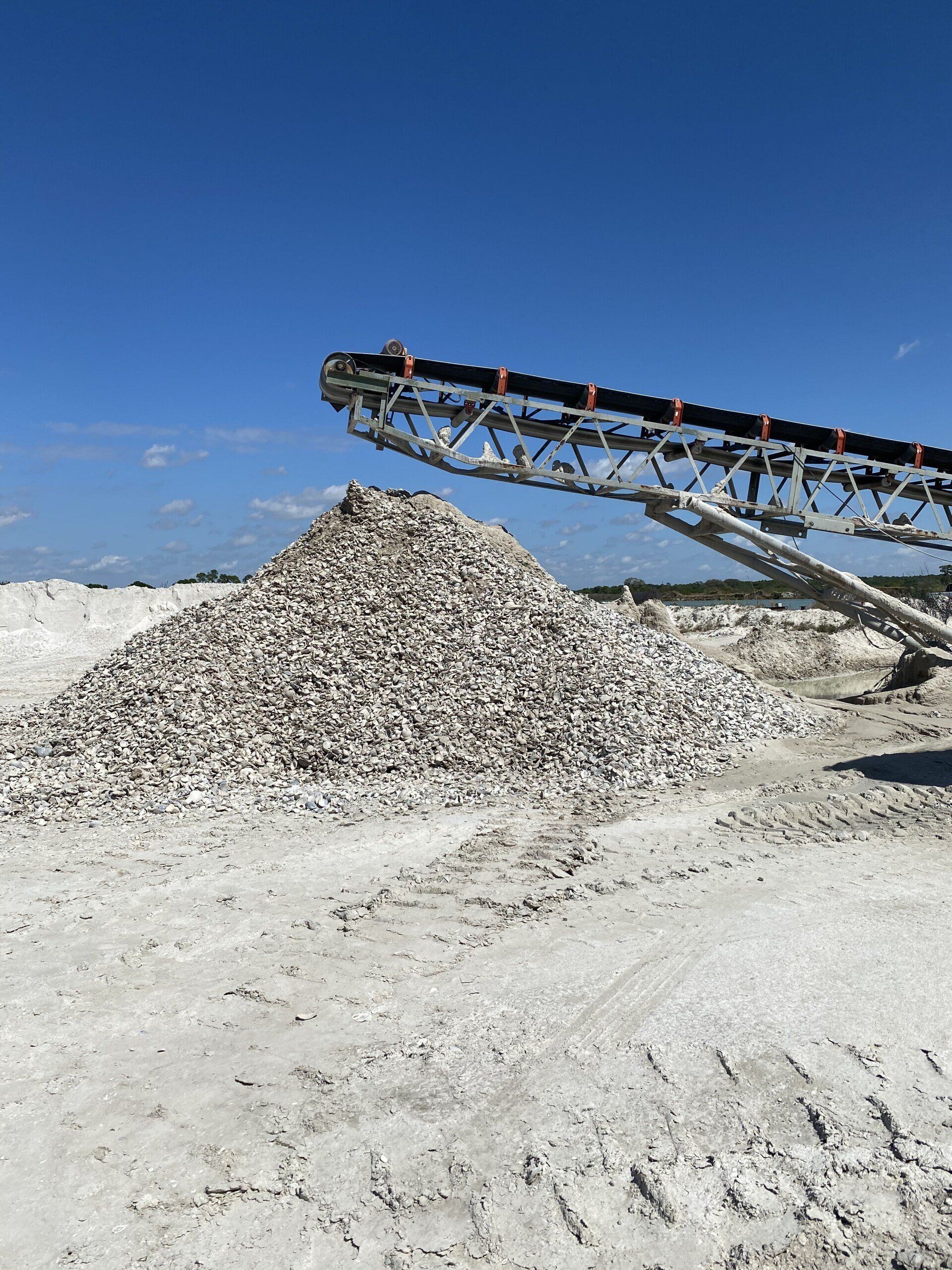 Conveyor unloading a large pile of crushed rock in a white quarry under a clear blue sky