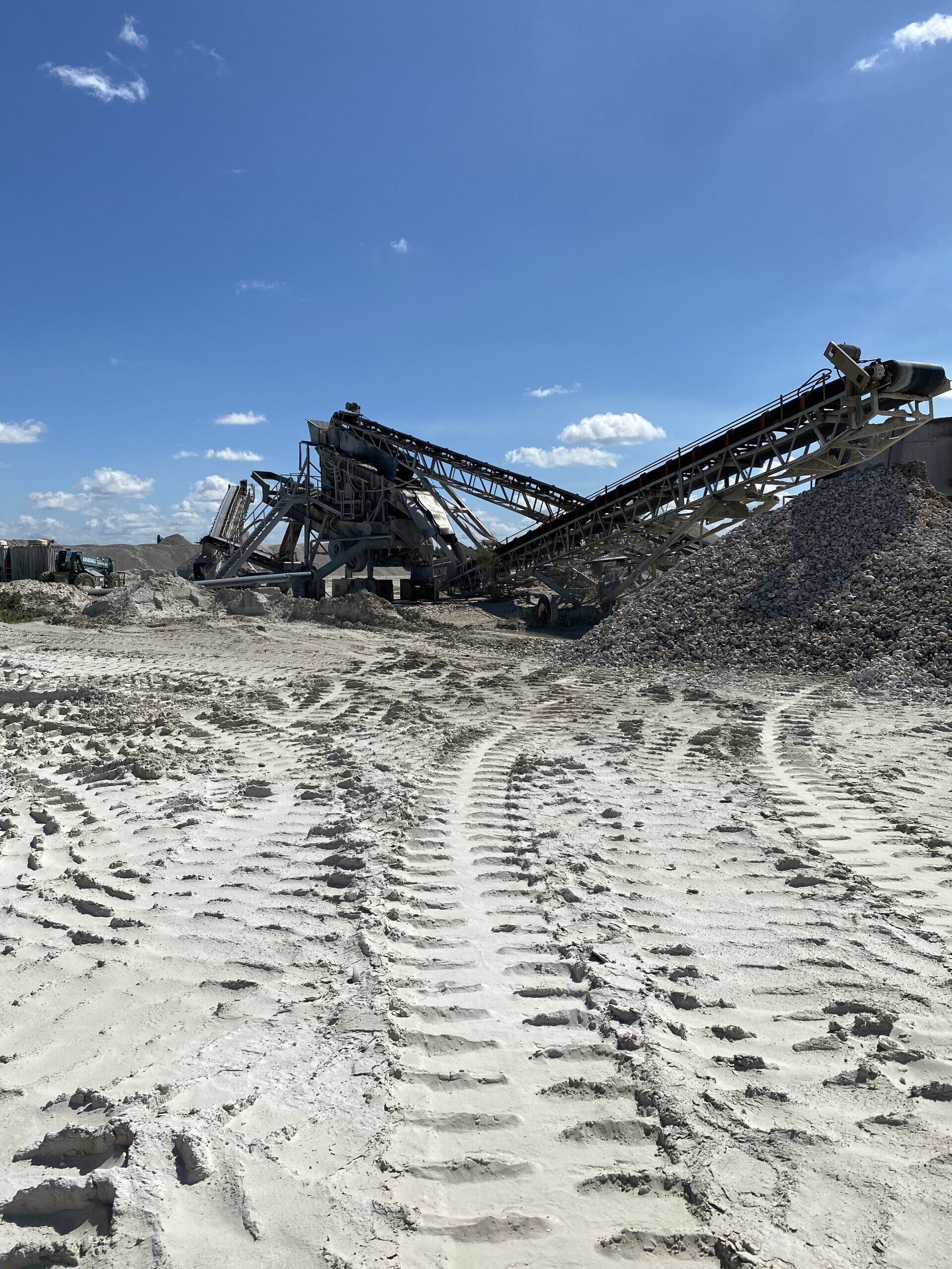 Large black industrial machine in a gravel quarry under a blue sky, with tire tracks in the foreground