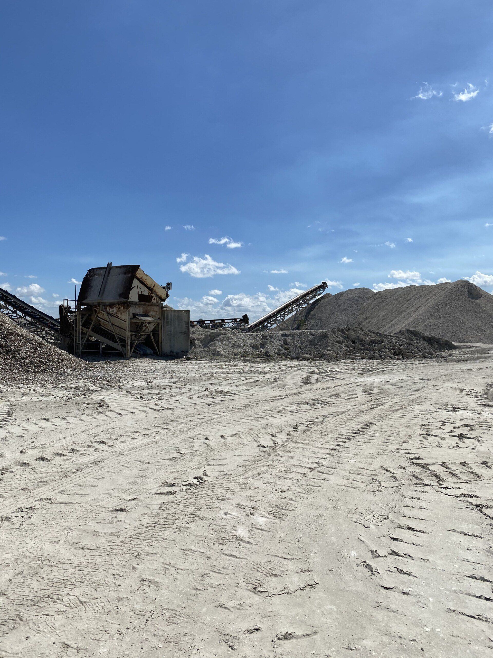 Gravel quarry with a conveyor and large piles under a bright blue sky