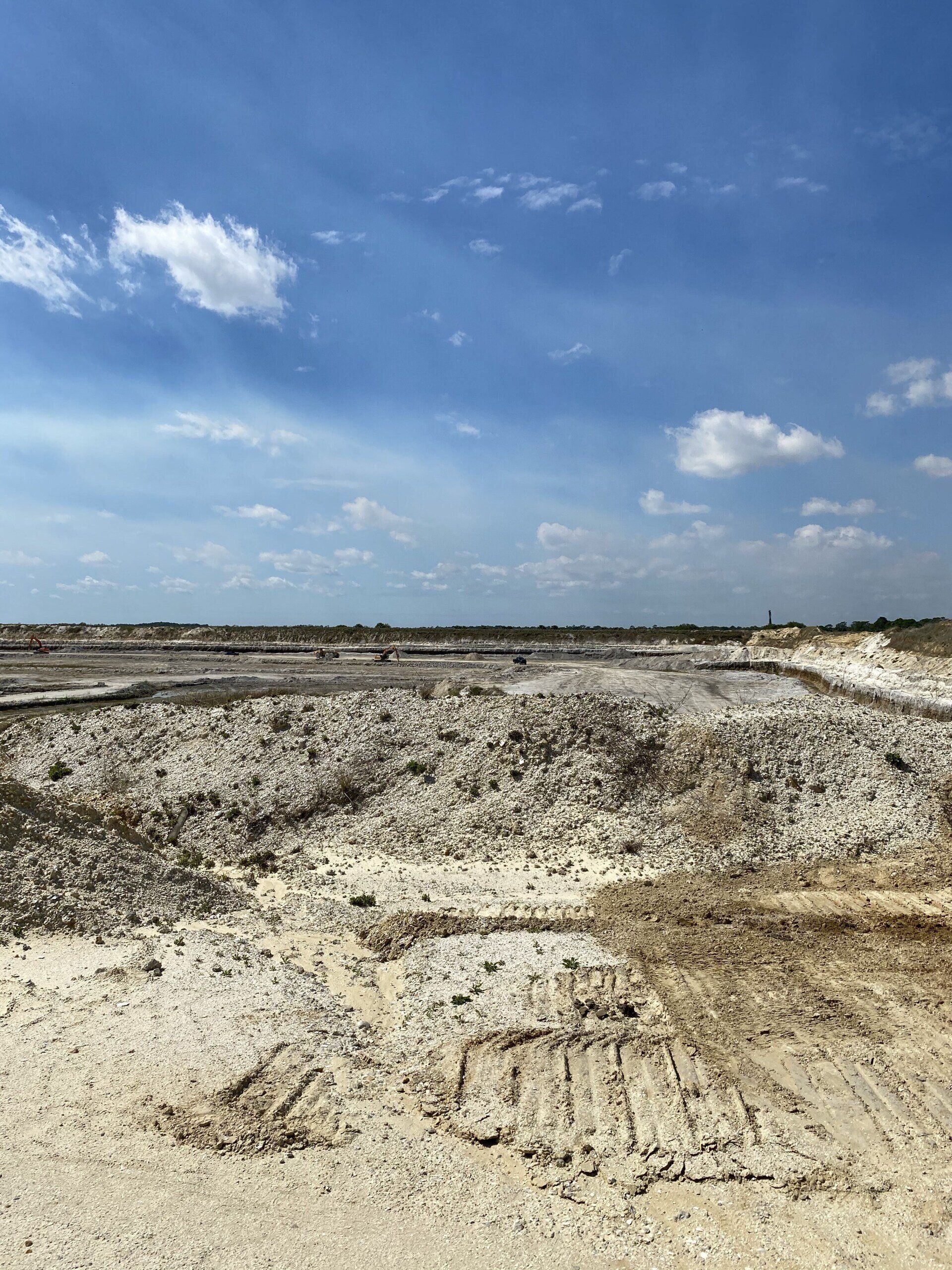 Barren excavation site with white dirt under a blue sky and scattered clouds