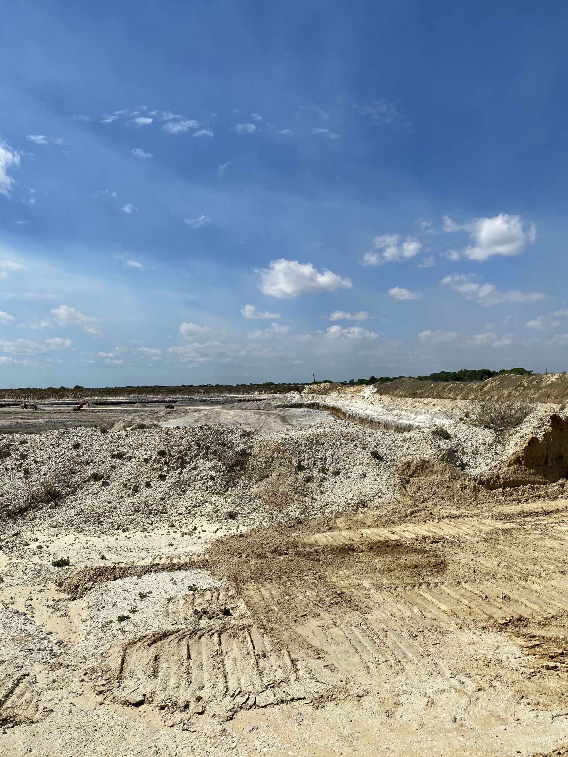 Wide sandy excavation site under a blue sky with scattered clouds