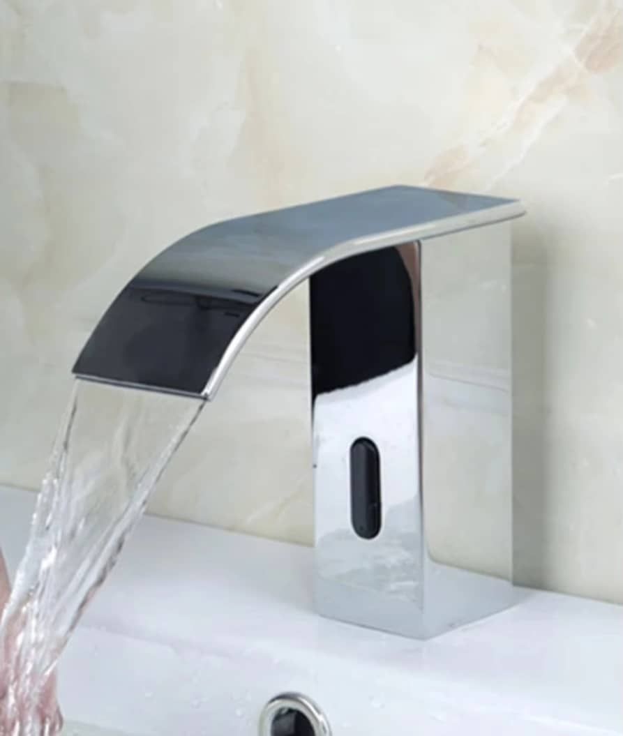 Grifo de baño cromado sobre lavabo blanco en un baño luminoso y minimalista.