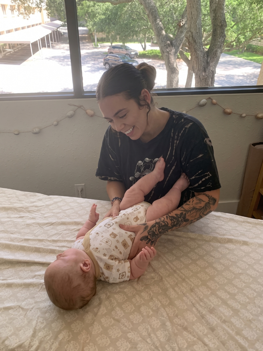 Adult hands holding a baby in a green onesie on a white quilted blanket