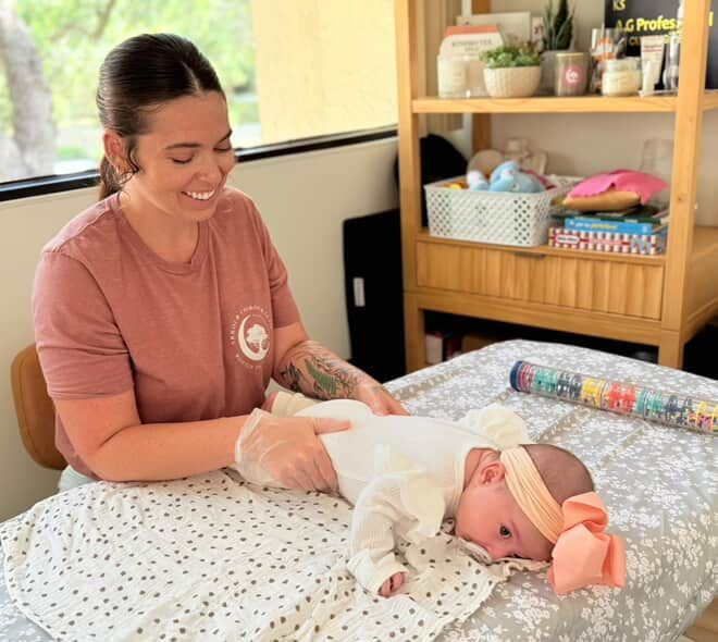 Caregiver smiling as she supports a baby lying on a patterned mat in a bright nursery
