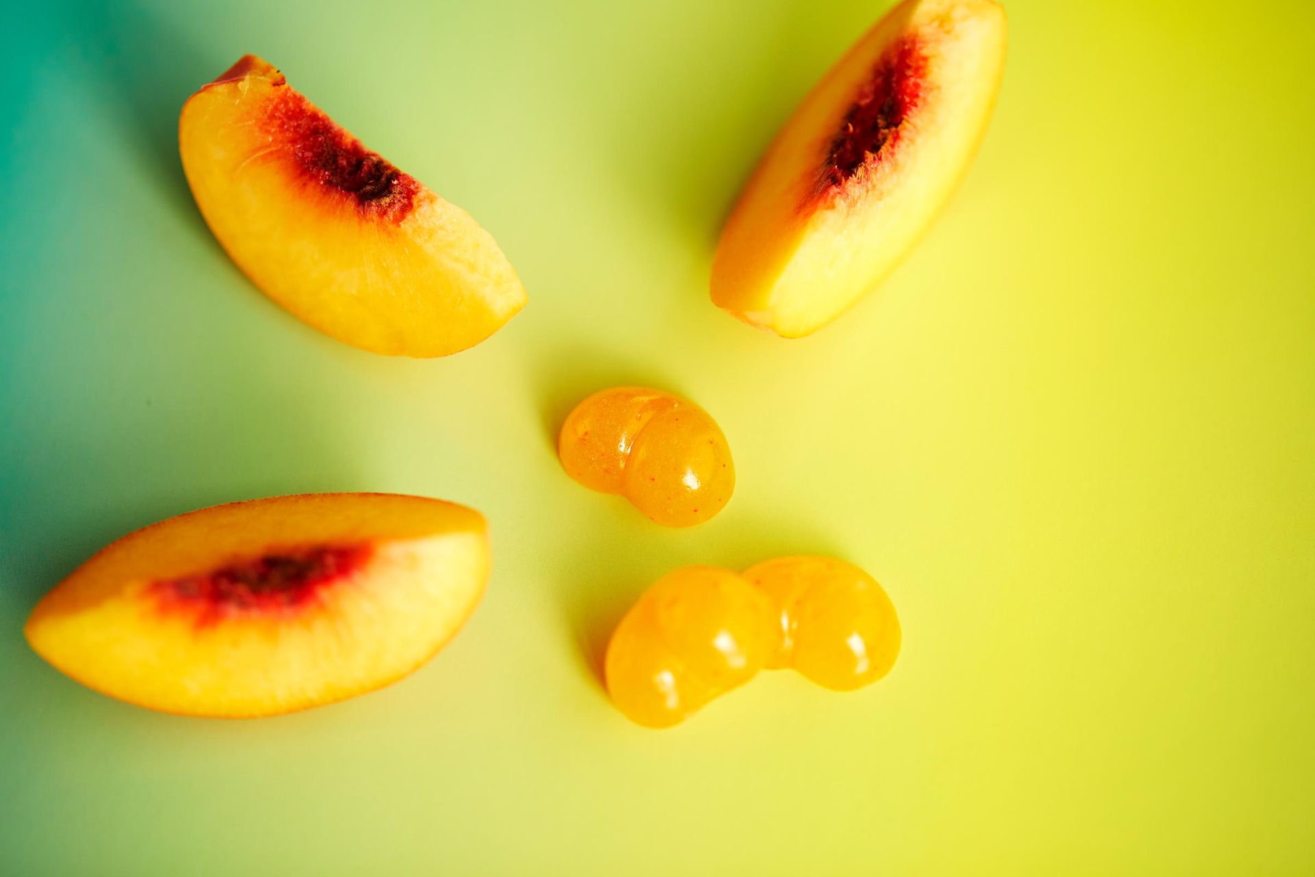 Sliced peaches and gummies on a yellow and green background.