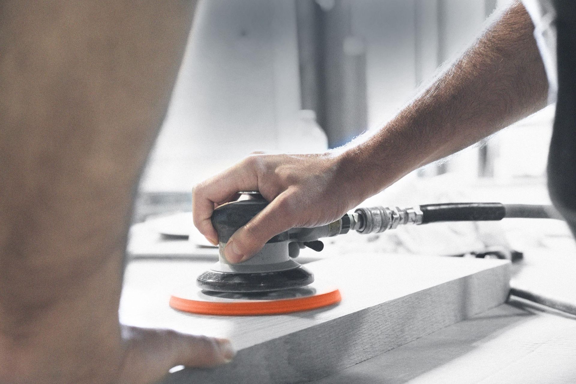 A person is sanding a piece of wood with an air sander.