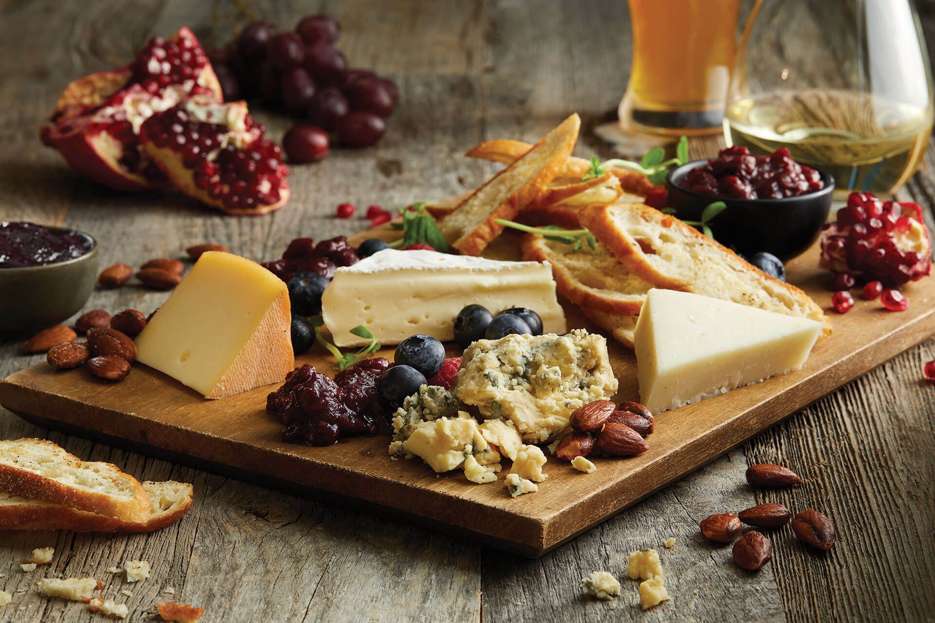 A wooden cutting board topped with cheese , fruit , nuts and bread.