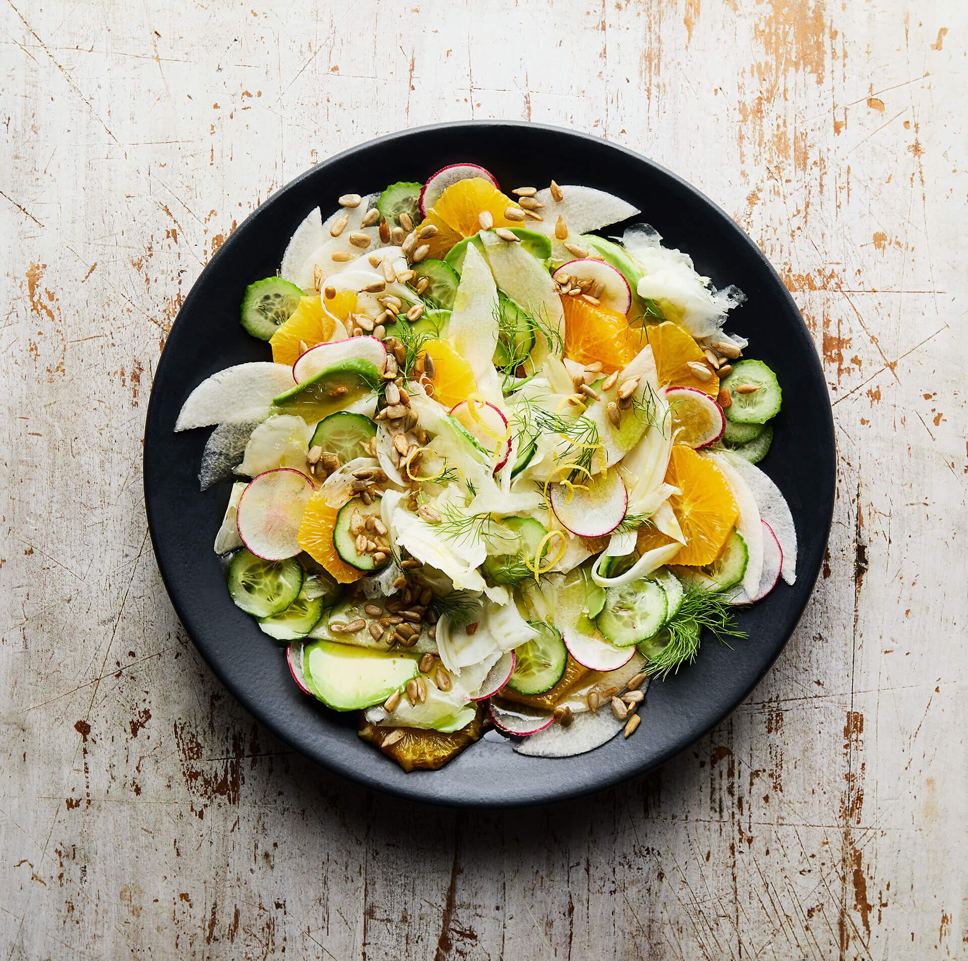 A salad on a black plate on a wooden table