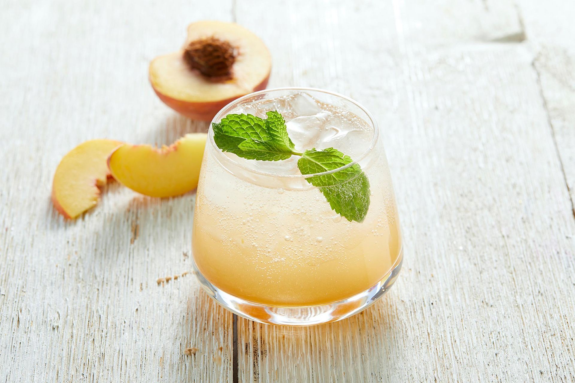 A glass of peach juice with ice and mint leaves on a wooden table.