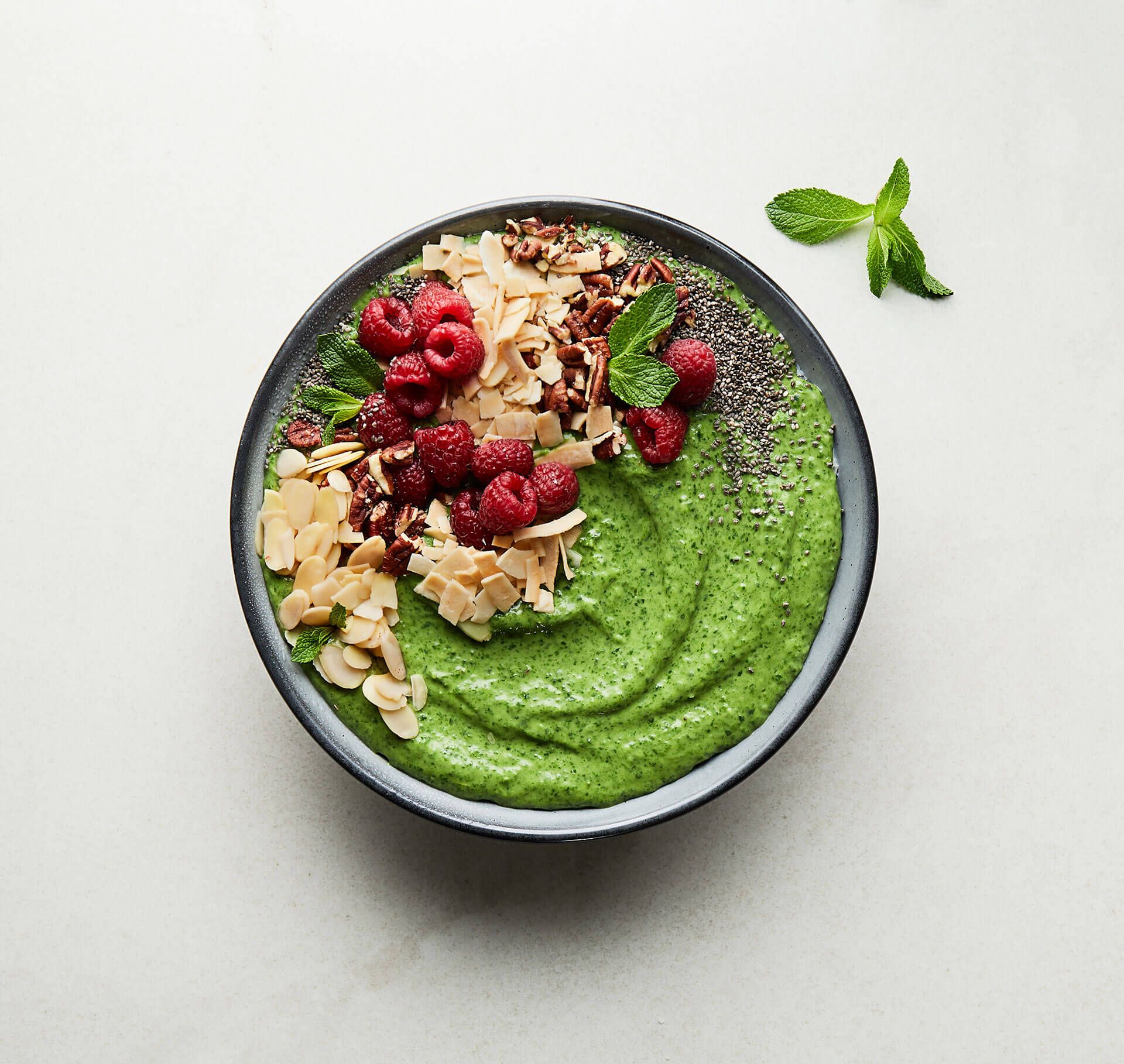 A bowl of green smoothie with raspberries , almonds and chia seeds.