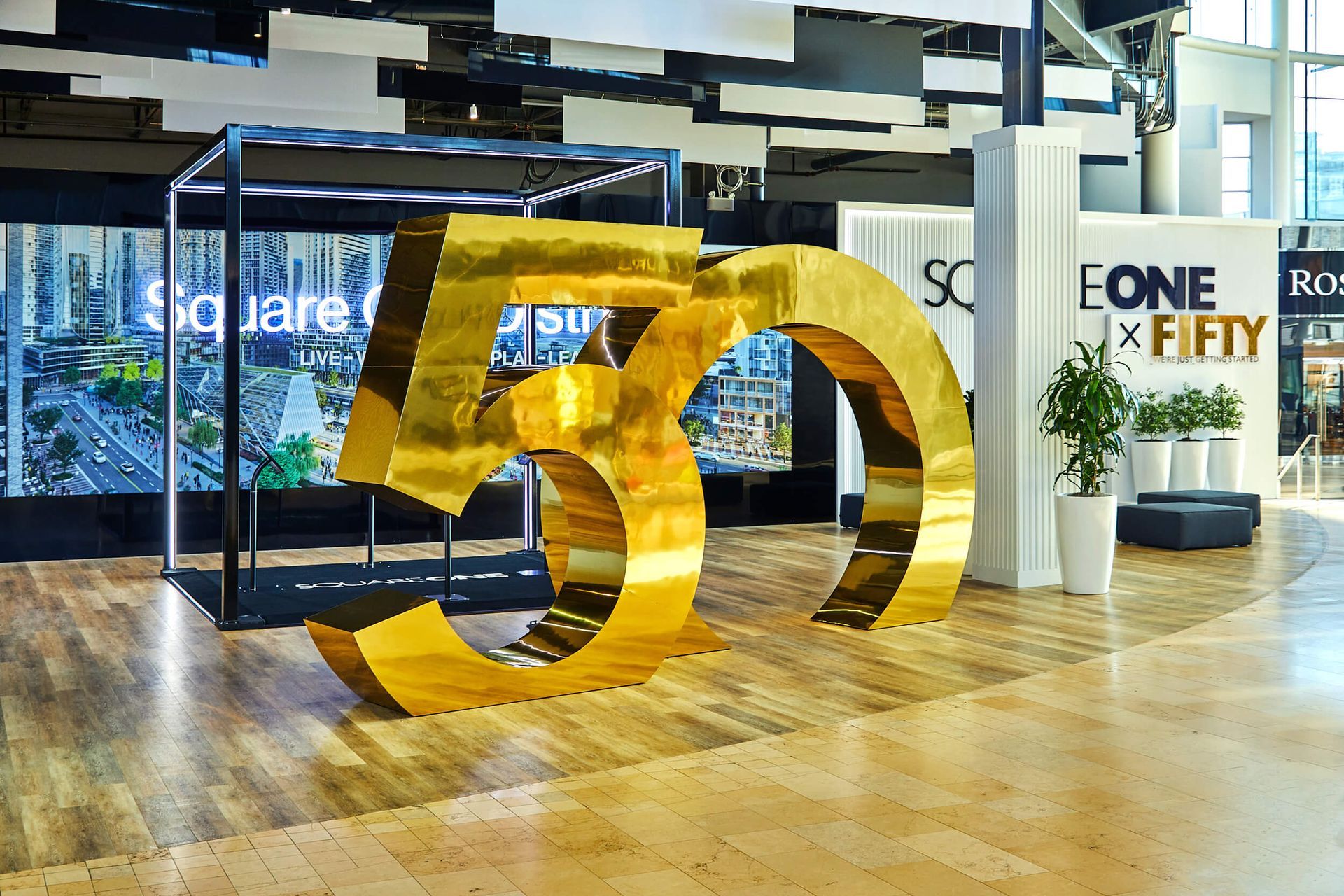 A large gold number 50 is sitting on a wooden floor in a lobby.