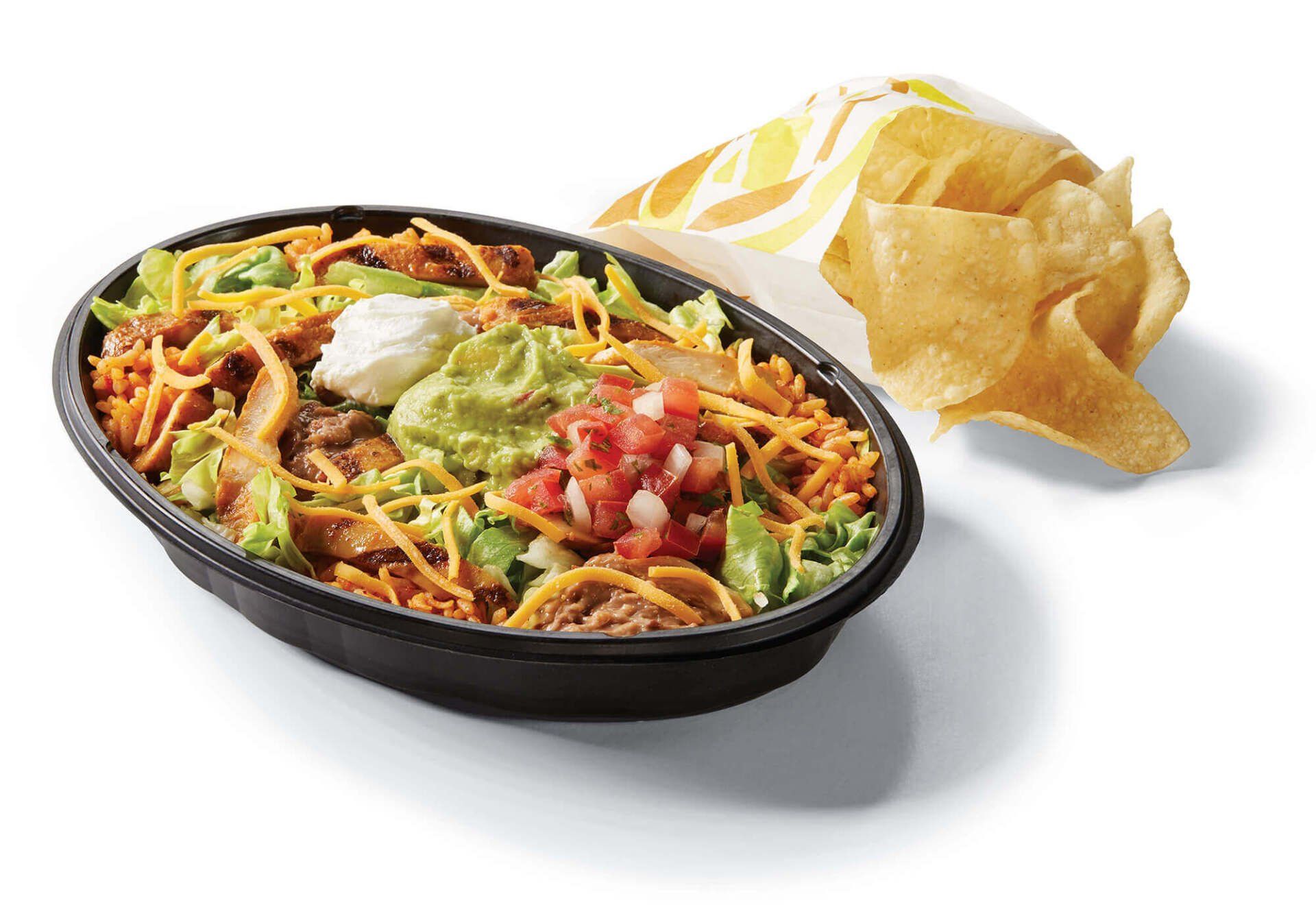 A bowl of taco bell food next to a bag of tortilla chips.