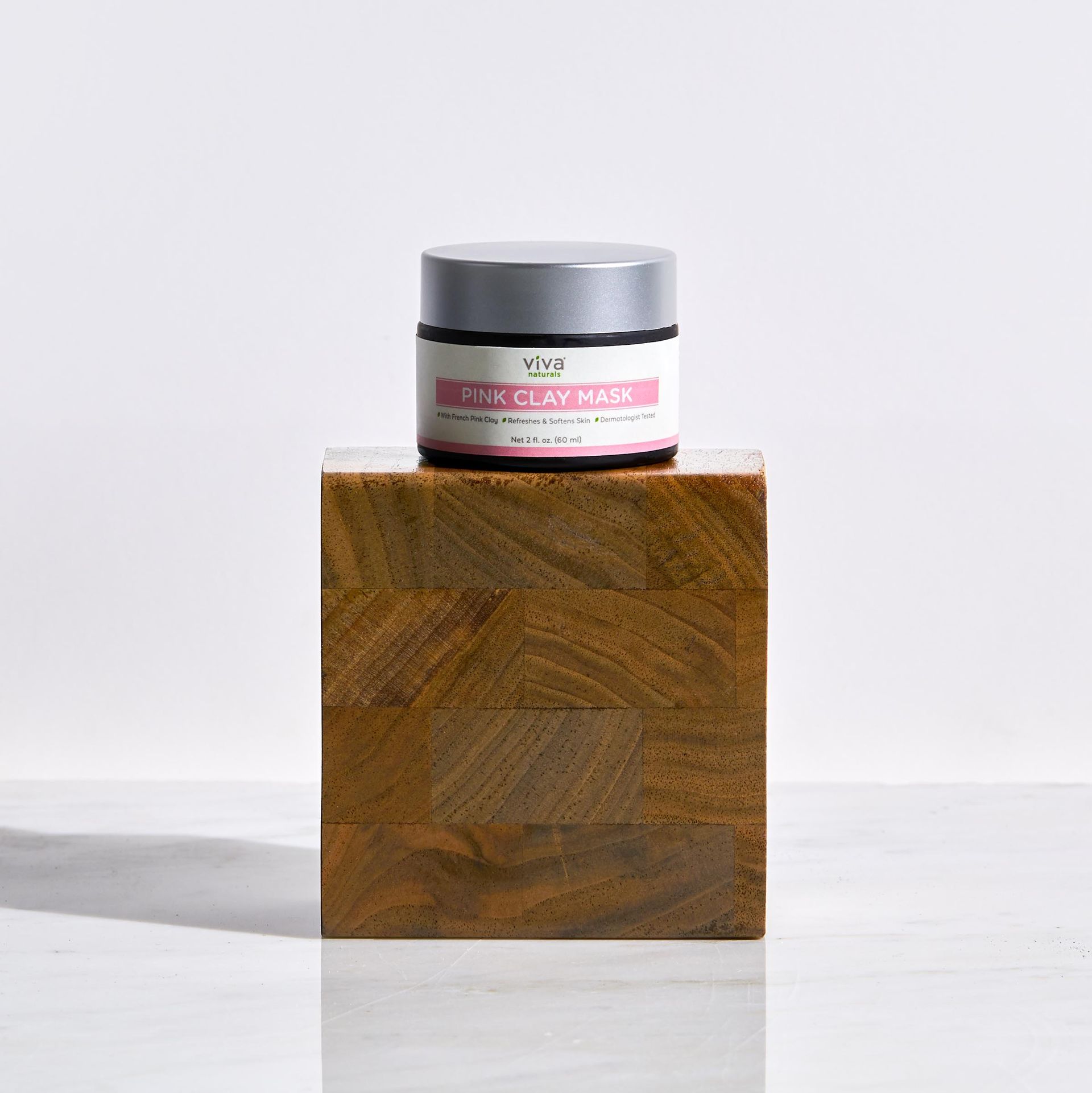 A jar of pink clay mask is sitting on top of a wooden block.