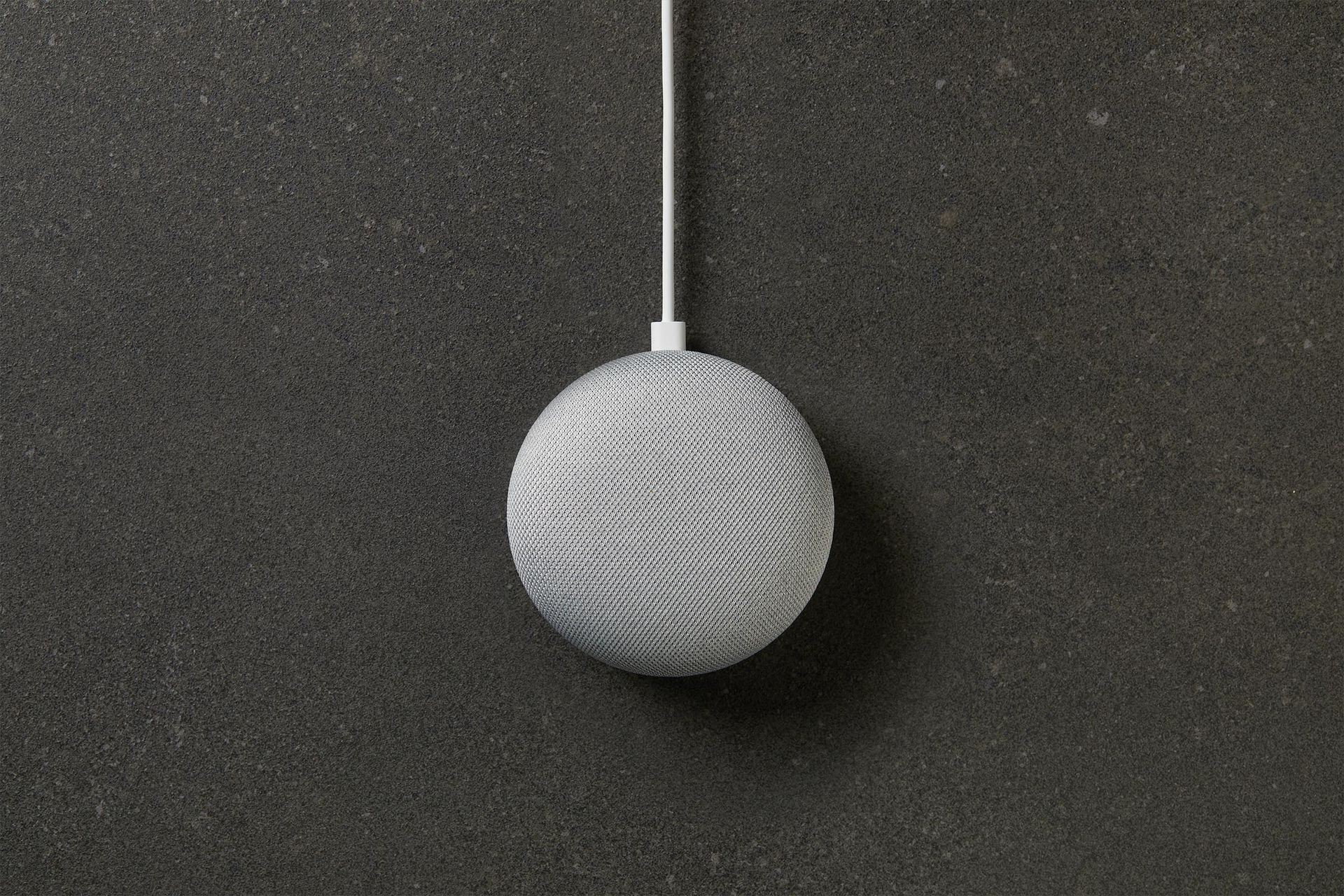 A smart speaker is hanging from a wire on a gray surface.
