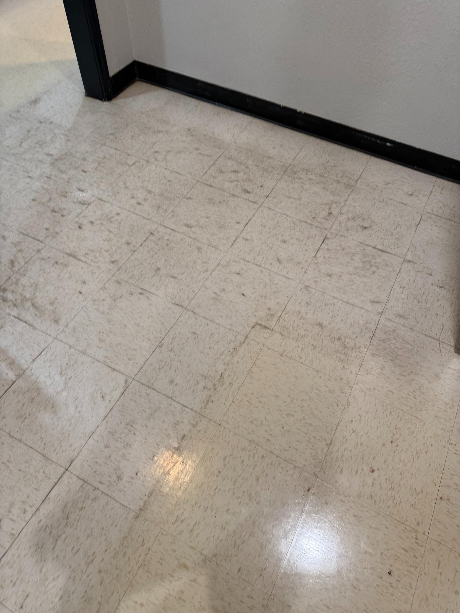 Light-speckled white tiled floor with black baseboards and wall corner.