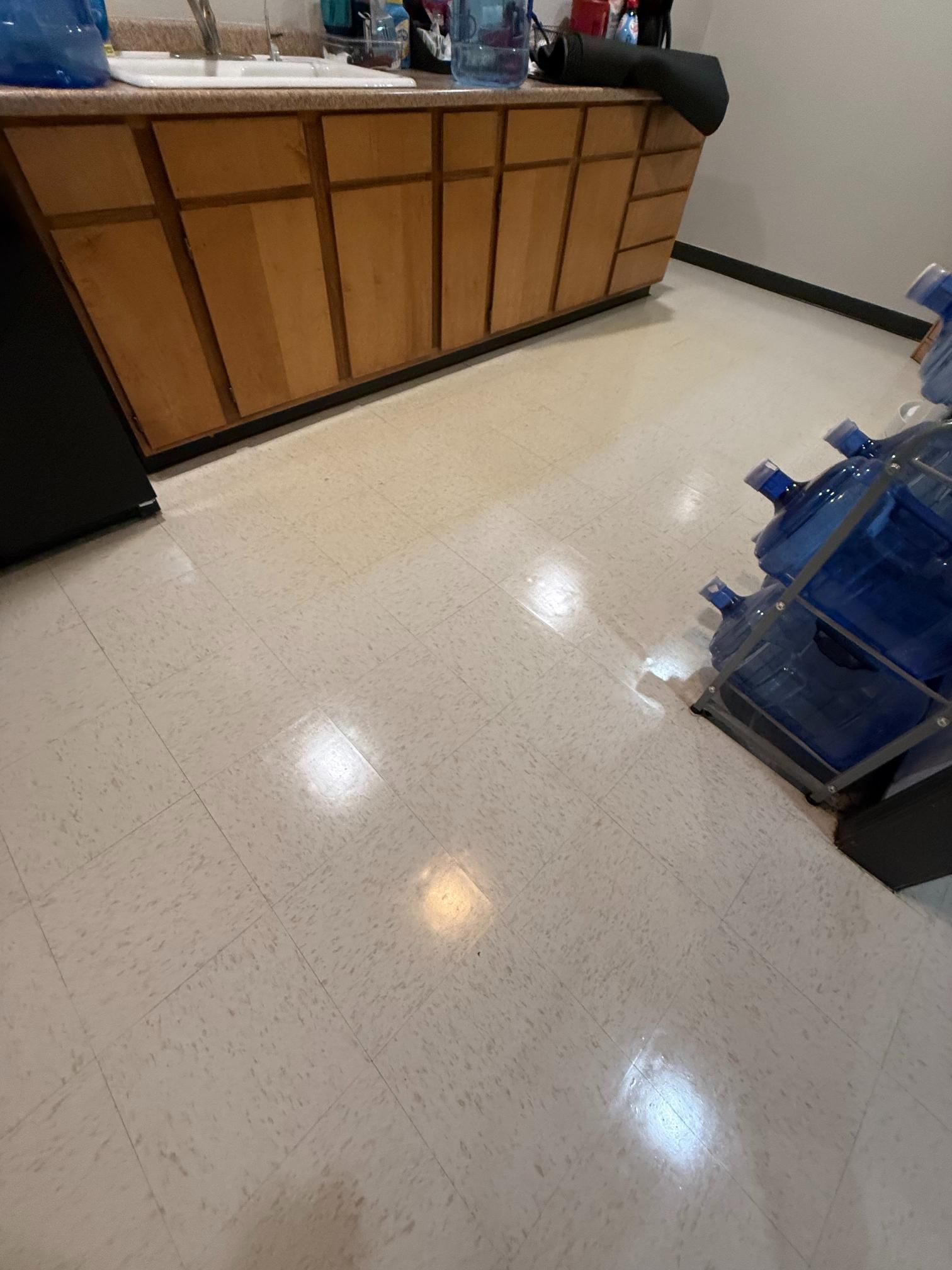 Empty office floor with glossy tile, wood reception counter, and a blue machine on the right.