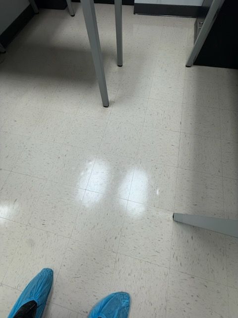 Blue shoes on a speckled floor beneath tables and chair legs in a room