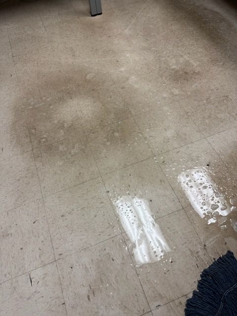 Scuffed light-gray tile floor with reflections and a dark blue rug edge in the corner