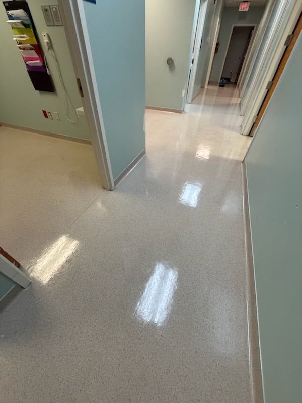 Empty hospital hallway with pale green walls and shiny beige floor, viewed through open doors.