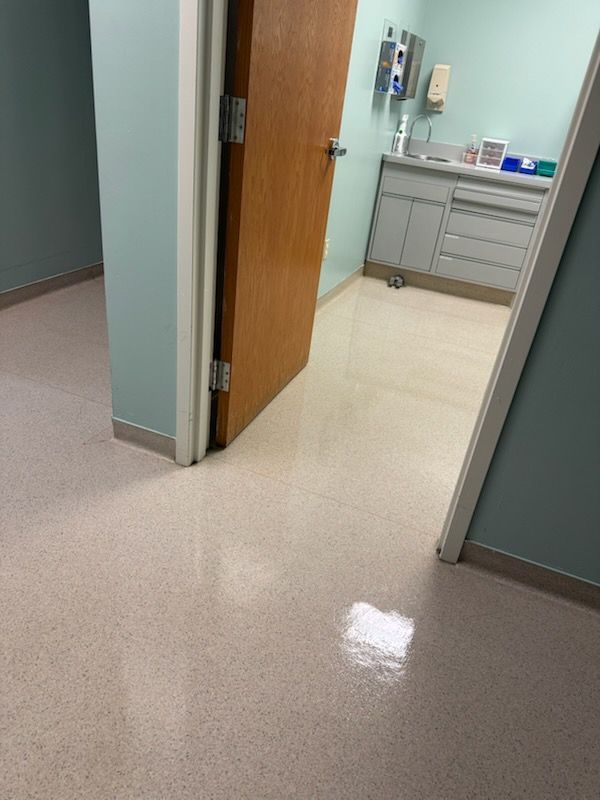 Open exam room doorway with beige floor and gray walls, leading to a sink and cabinets inside.