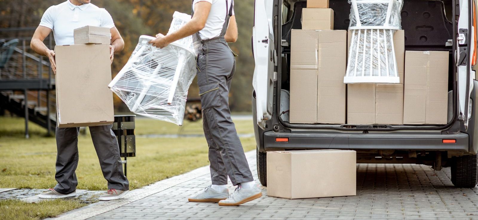 Two people loading boxes and furniture into a van on a driveway.