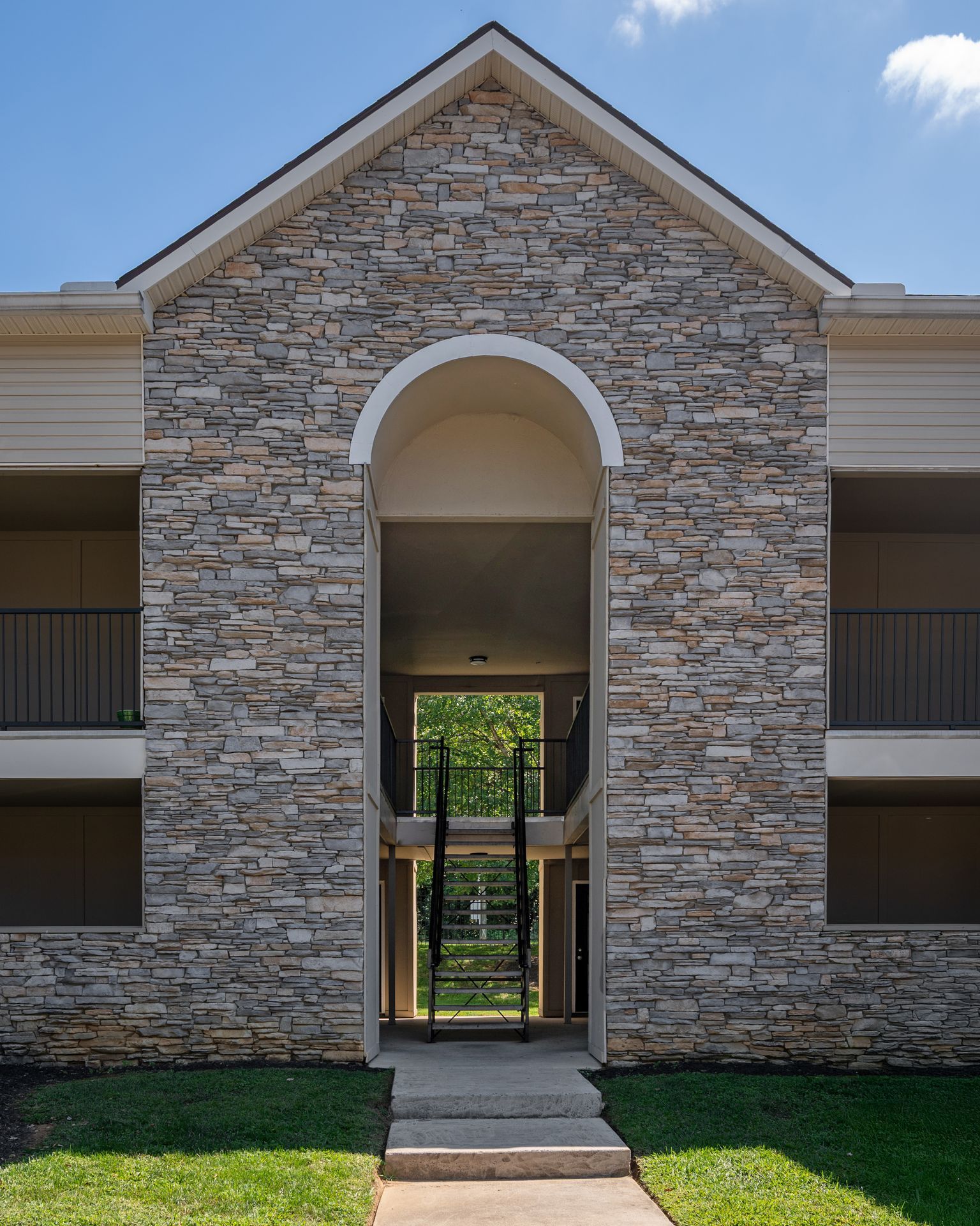 Stone apartment building entrance with central archway and walkway to courtyard