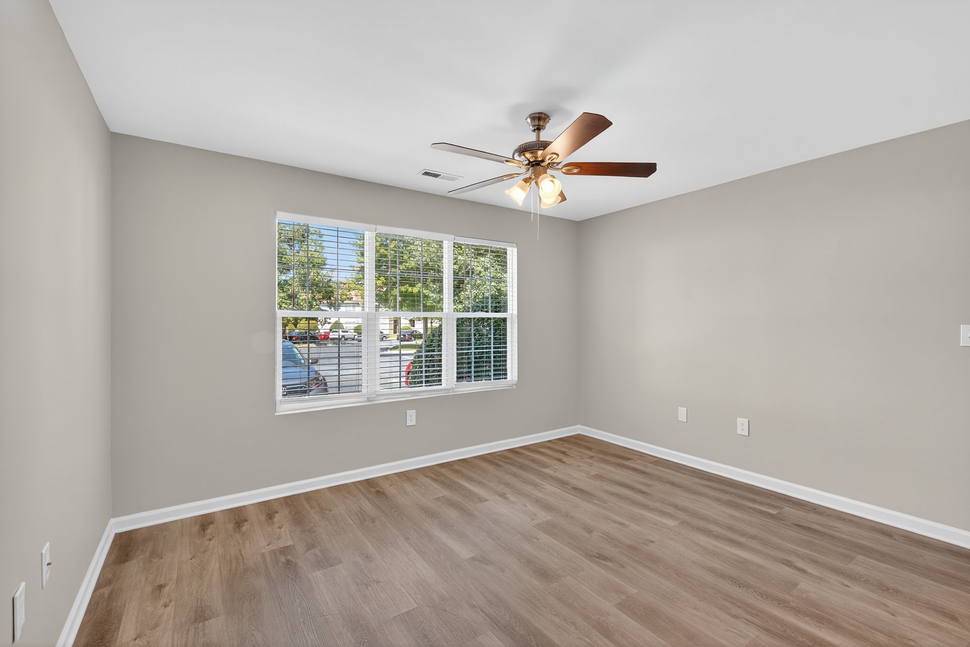 Empty bedroom with gray walls, wood-look floors, ceiling fan, and a large window.