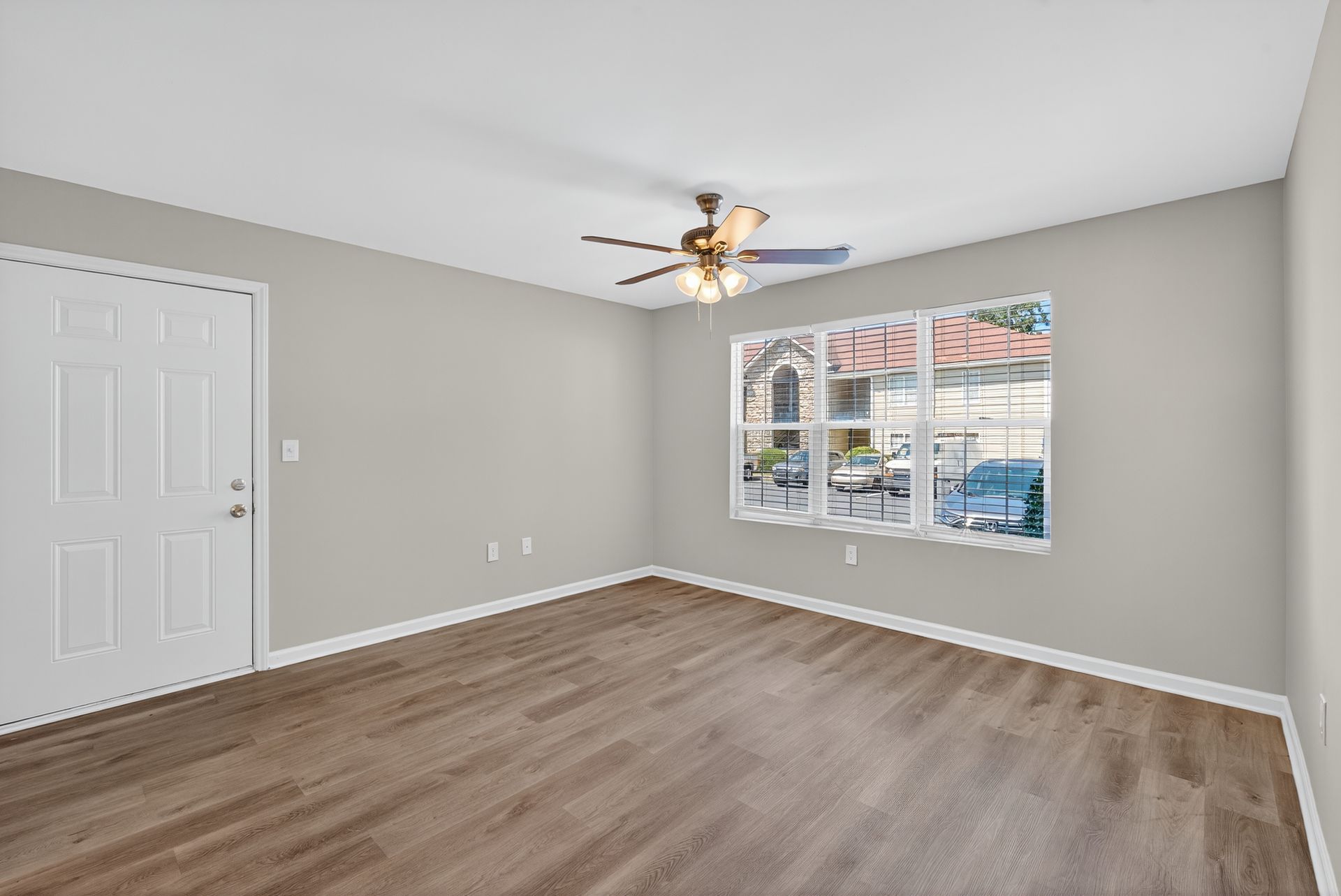 Empty gray bedroom with wood-look flooring, ceiling fan, and a large window with blinds.