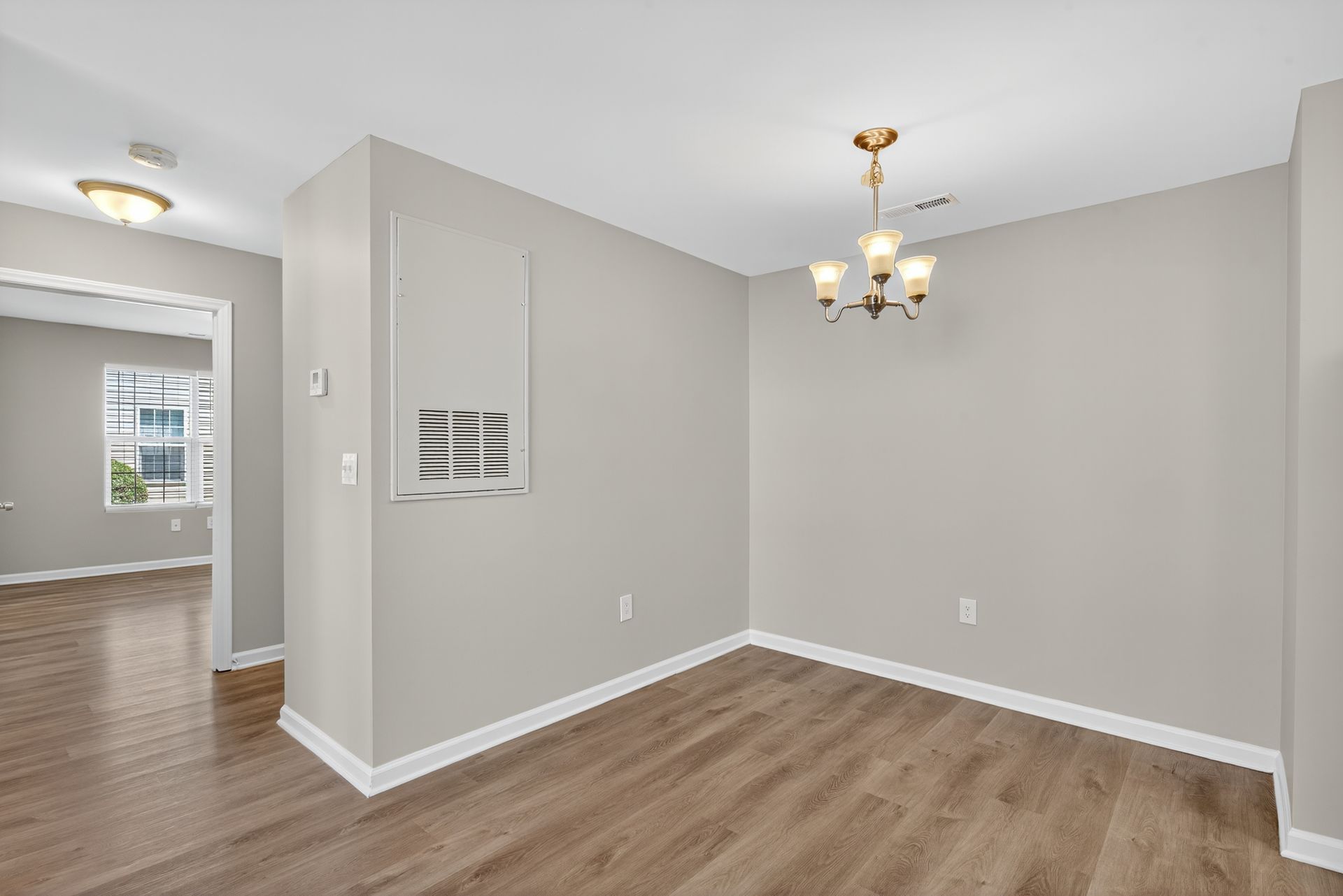 Empty dining room with light gray walls, wood flooring, and a small chandelier near an open doorway.