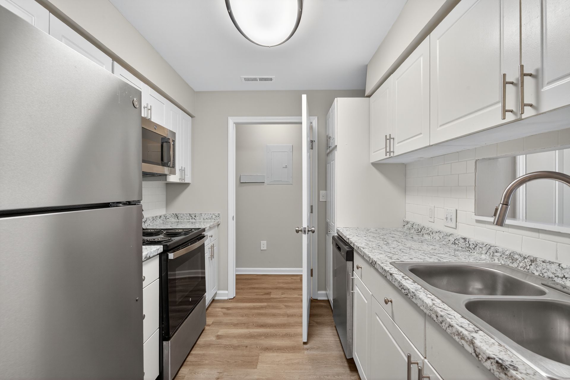 Narrow white kitchen with stainless steel appliances, white cabinets, and granite countertops