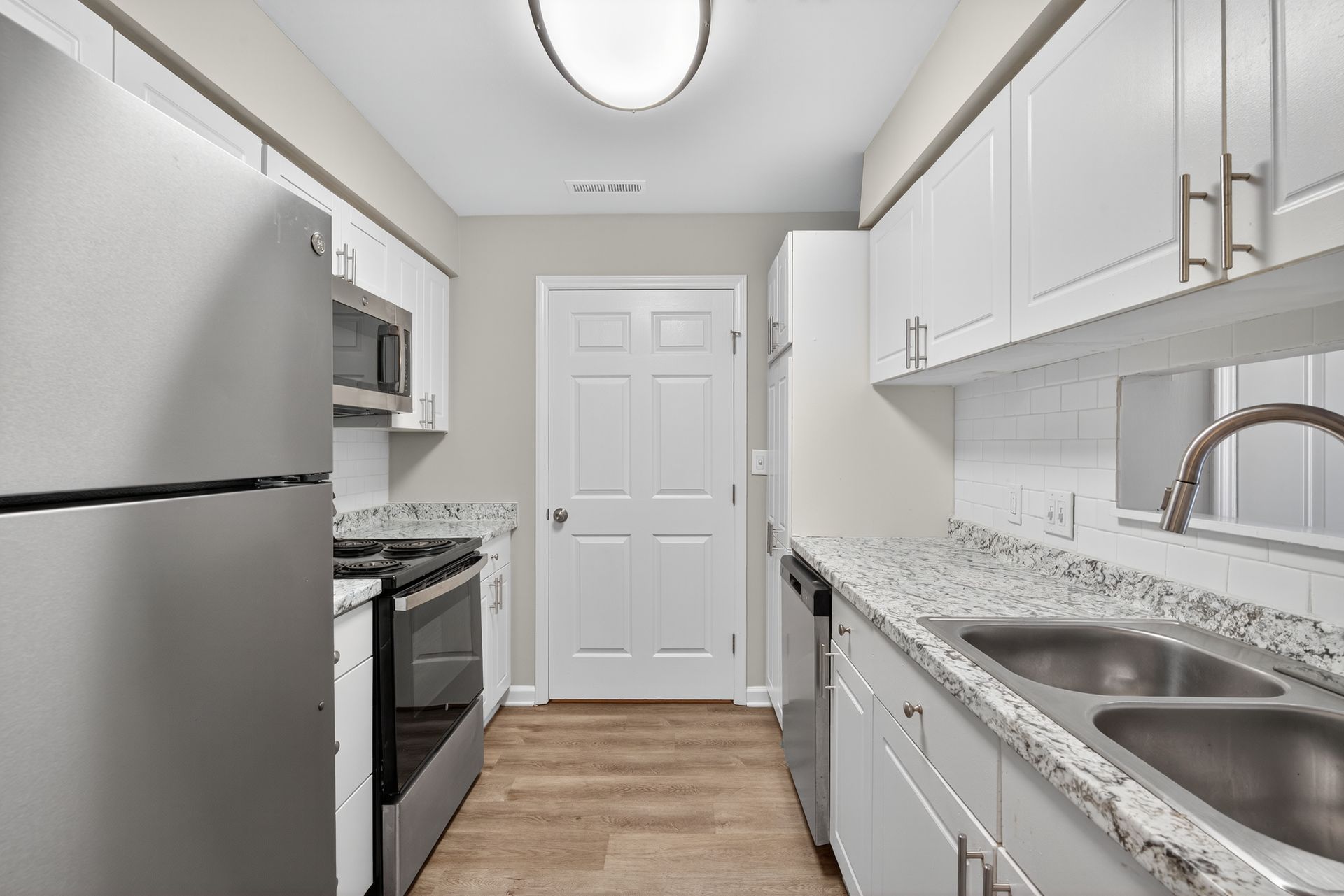 Bright white galley kitchen with stainless appliances, granite countertops, and wood floor