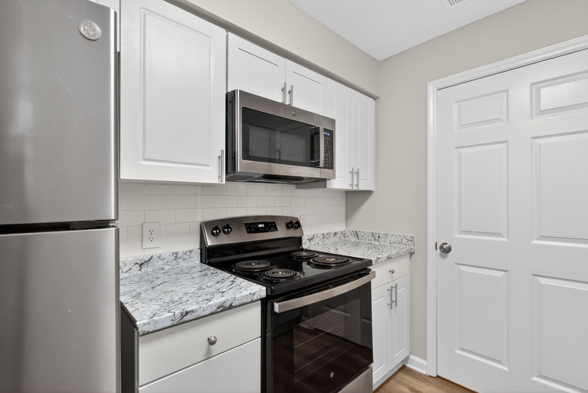 Compact kitchen with stainless steel appliances, white cabinets, and gray granite countertop