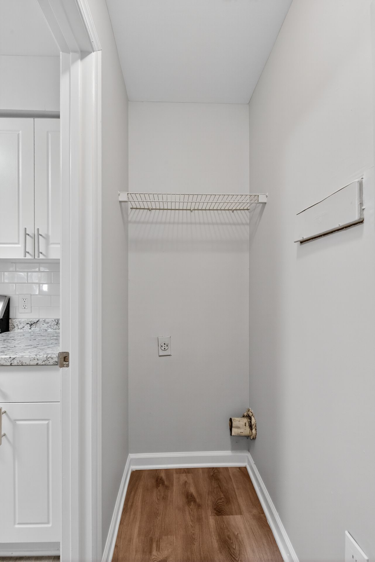 Empty laundry closet with white walls, wire shelf, and wood-look floor, viewed from a doorway