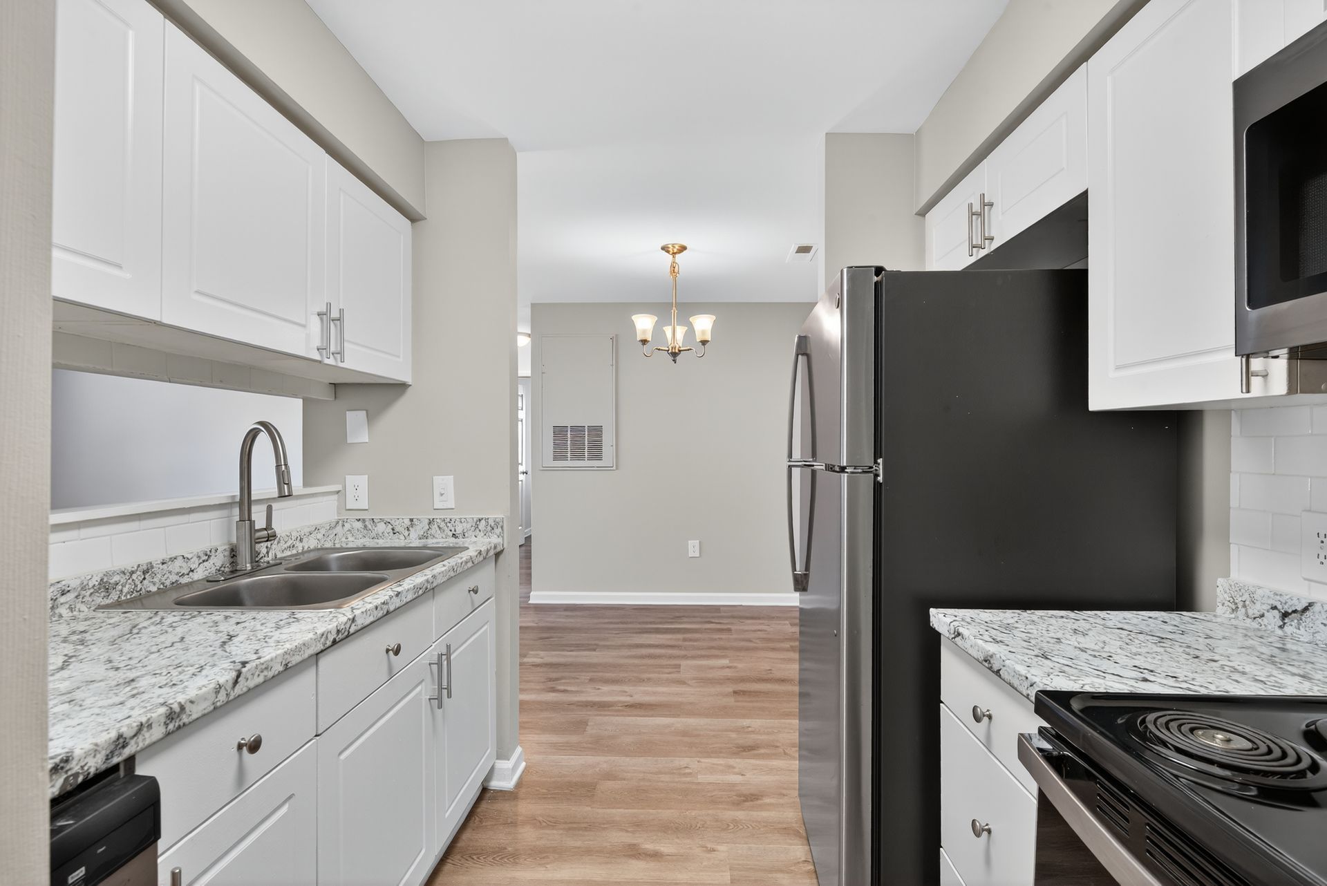 Bright kitchen with white cabinets, granite counters, stainless fridge, and wood floors